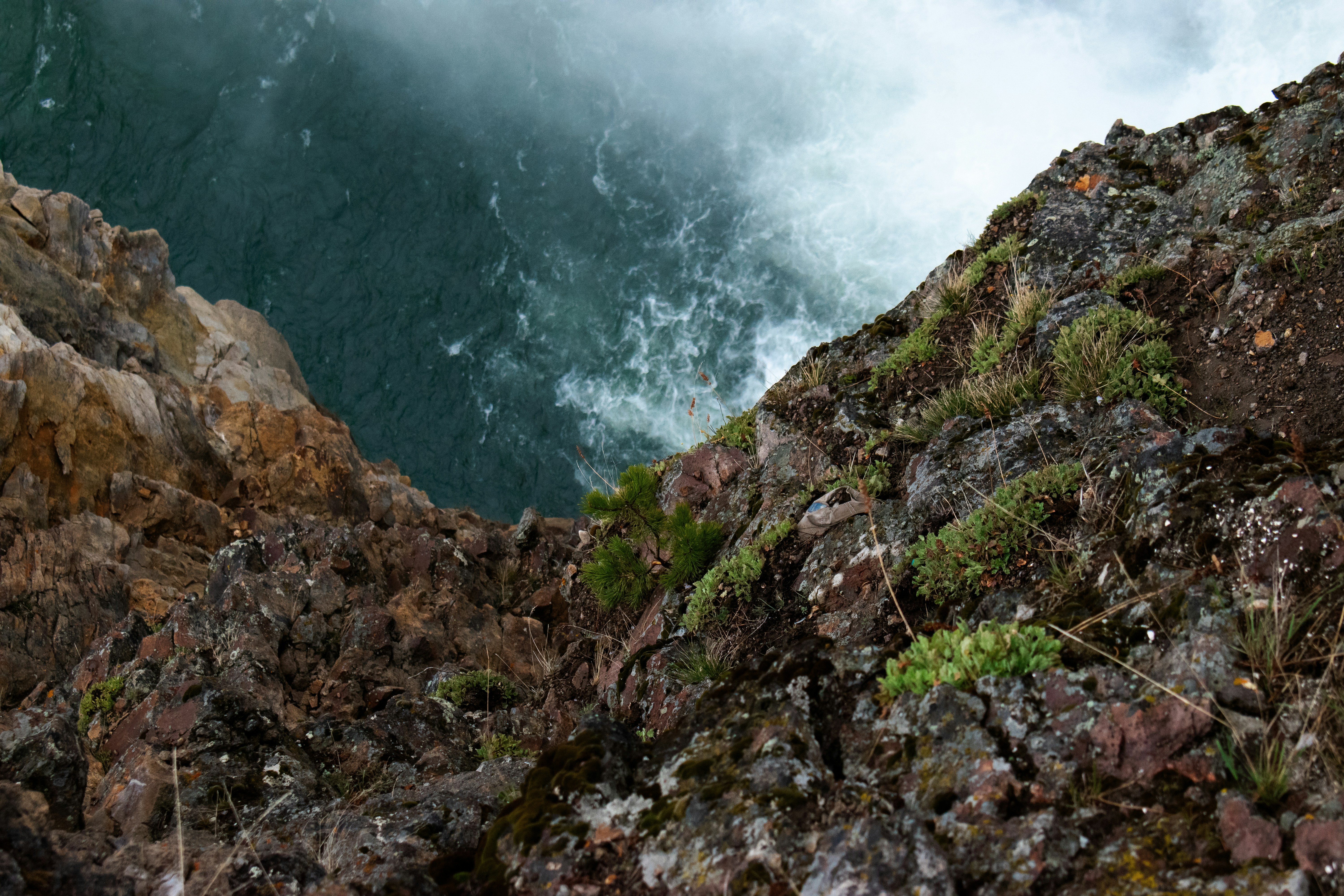 Steep rocky cliff overlooking turbulent green water.