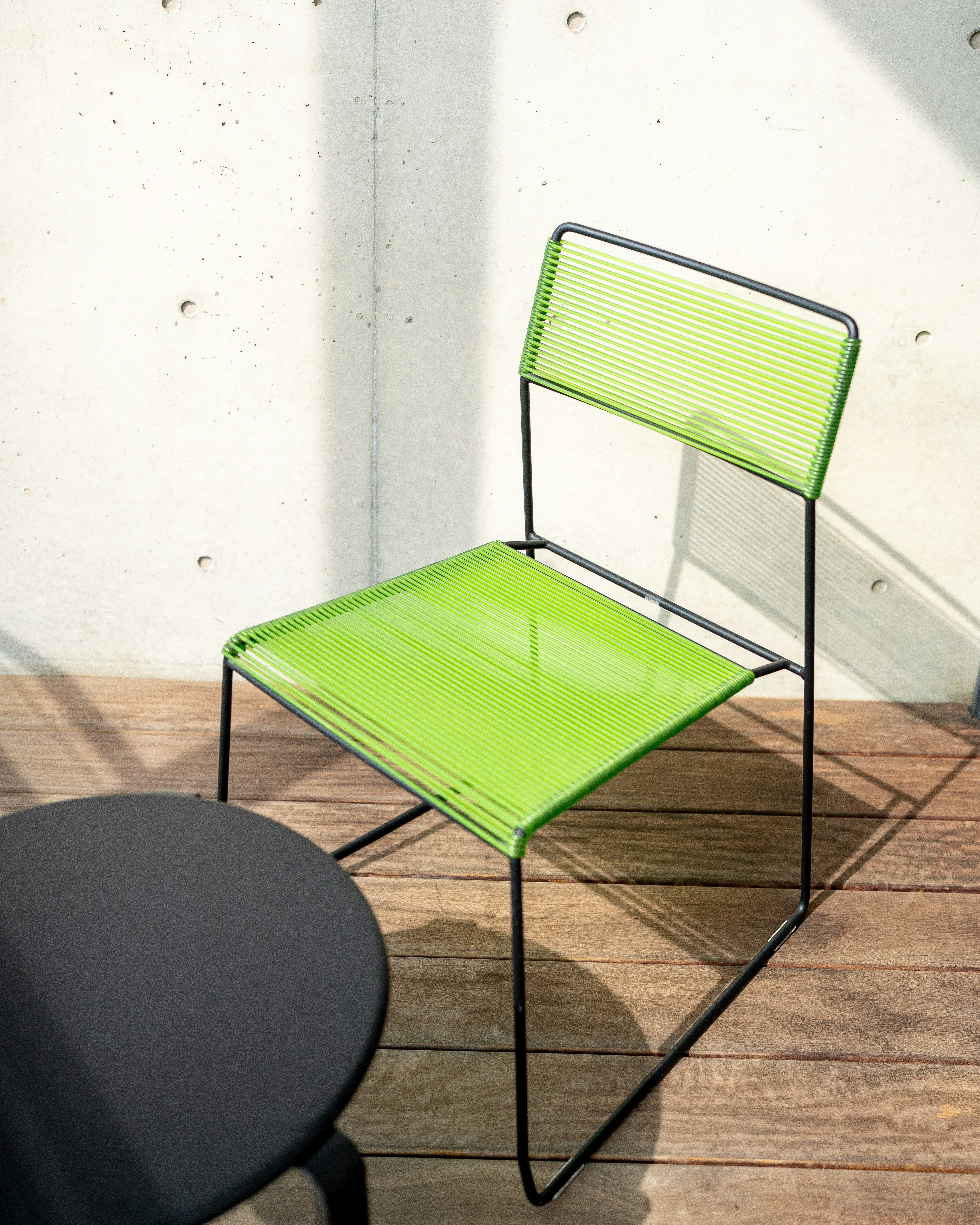 Modern green chair and black table on a wooden deck.