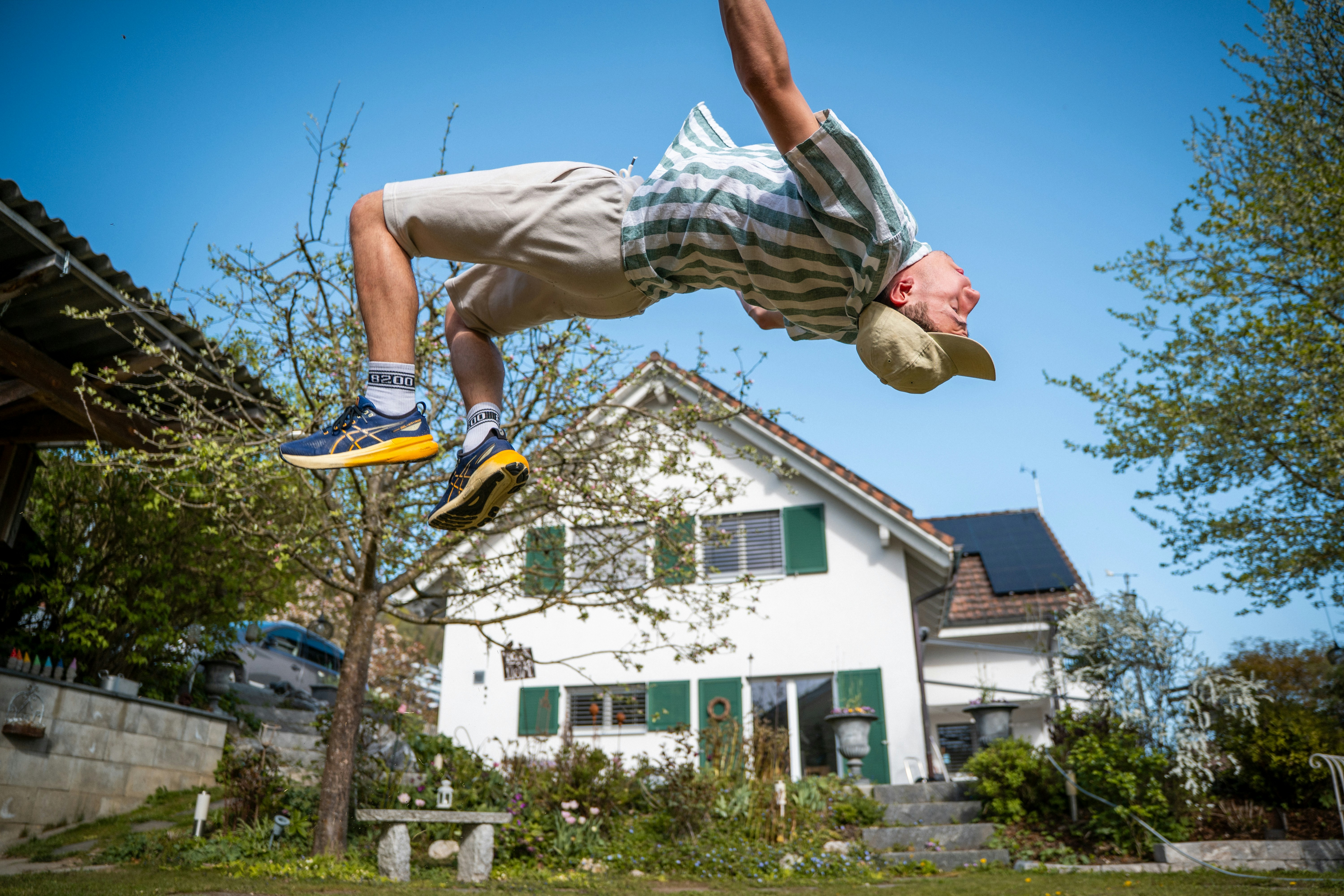 Energetic man doing a backflip in a sunny garden.