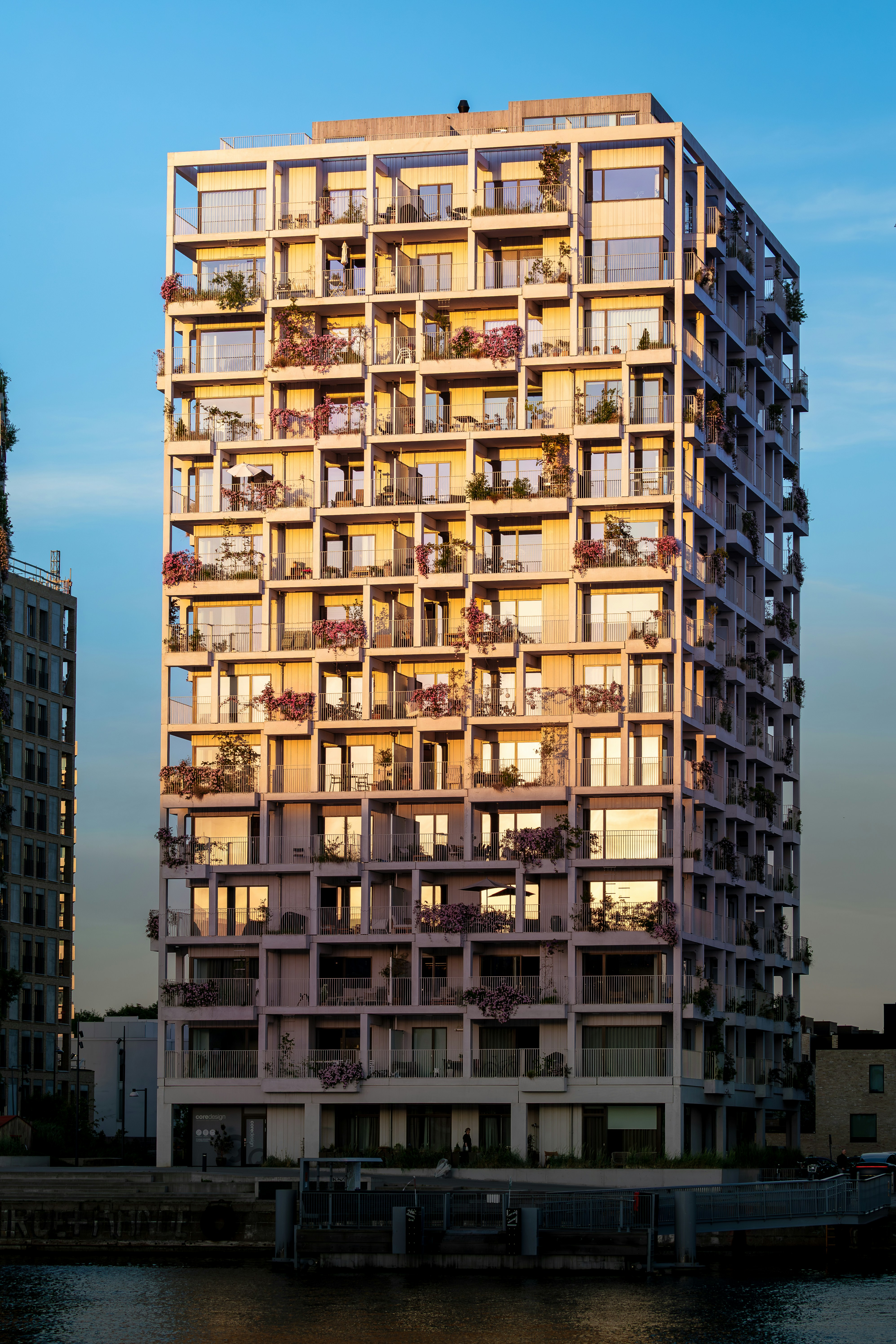 Edifício residencial moderno com muitas varandas e plantas à beira da água.