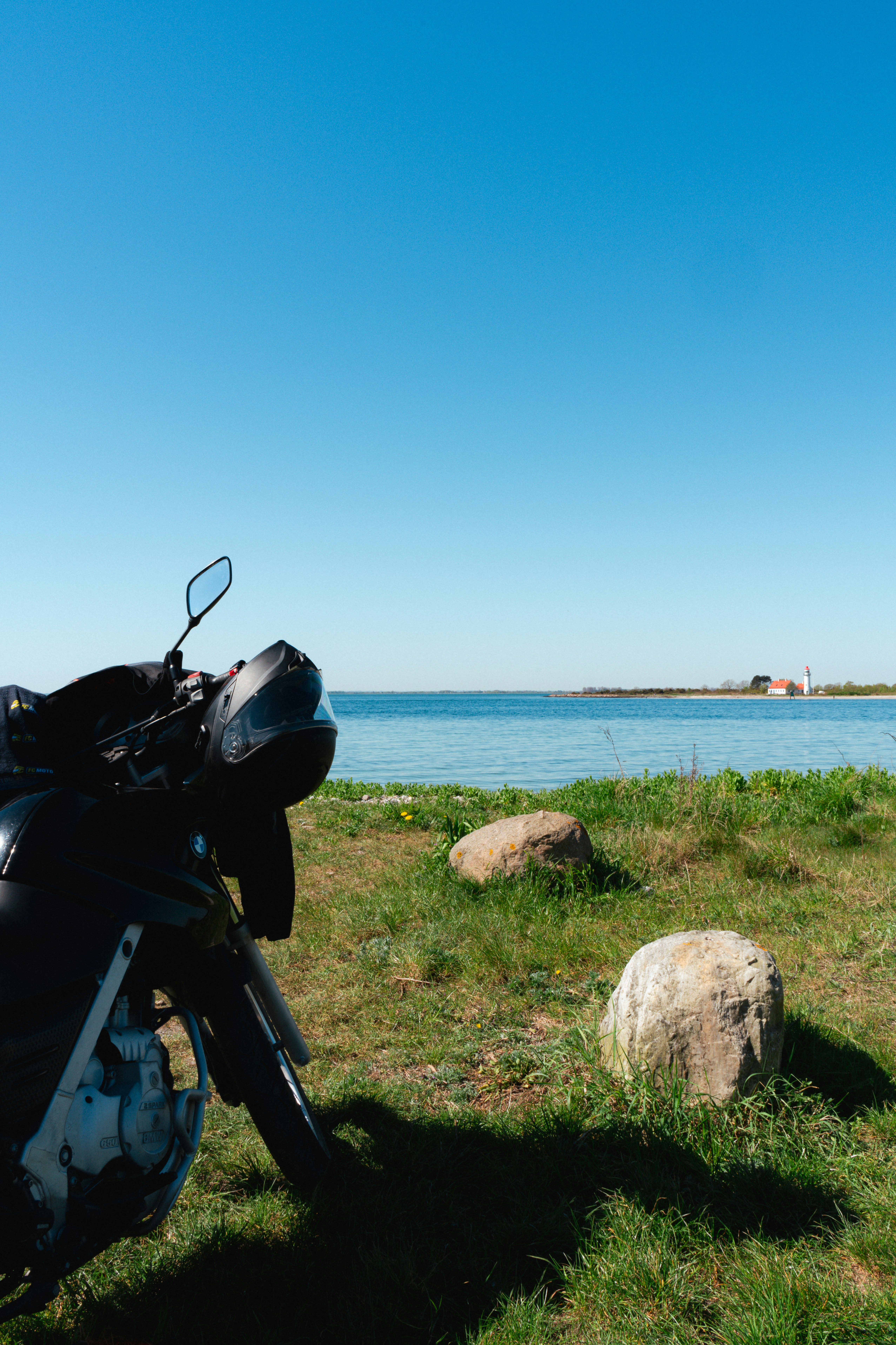 Moto negra aparcada en la orilla de hierba con vistas a aguas azules y tranquilas