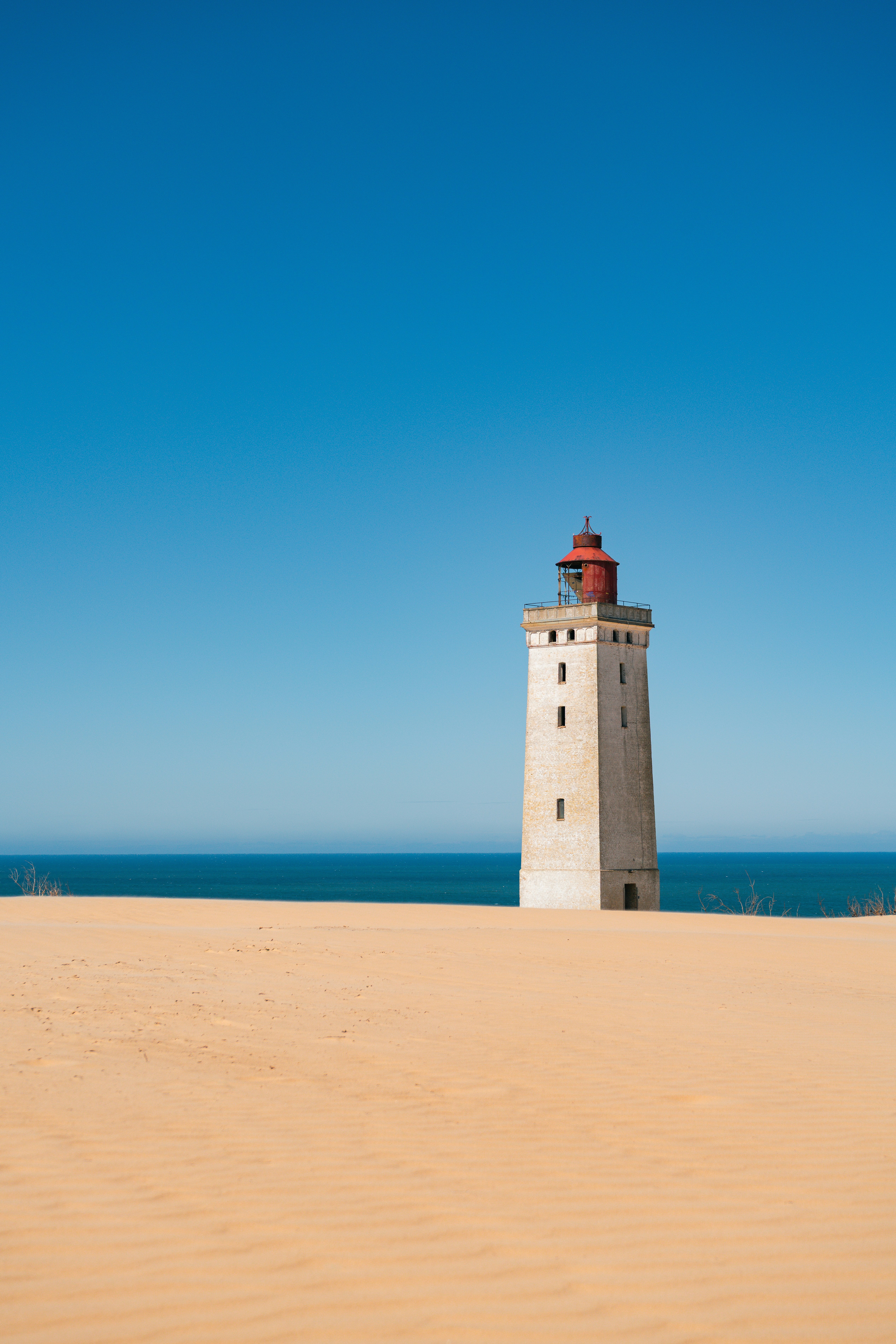 Historic lighthouse on vast sand dunes under clear blue sky.