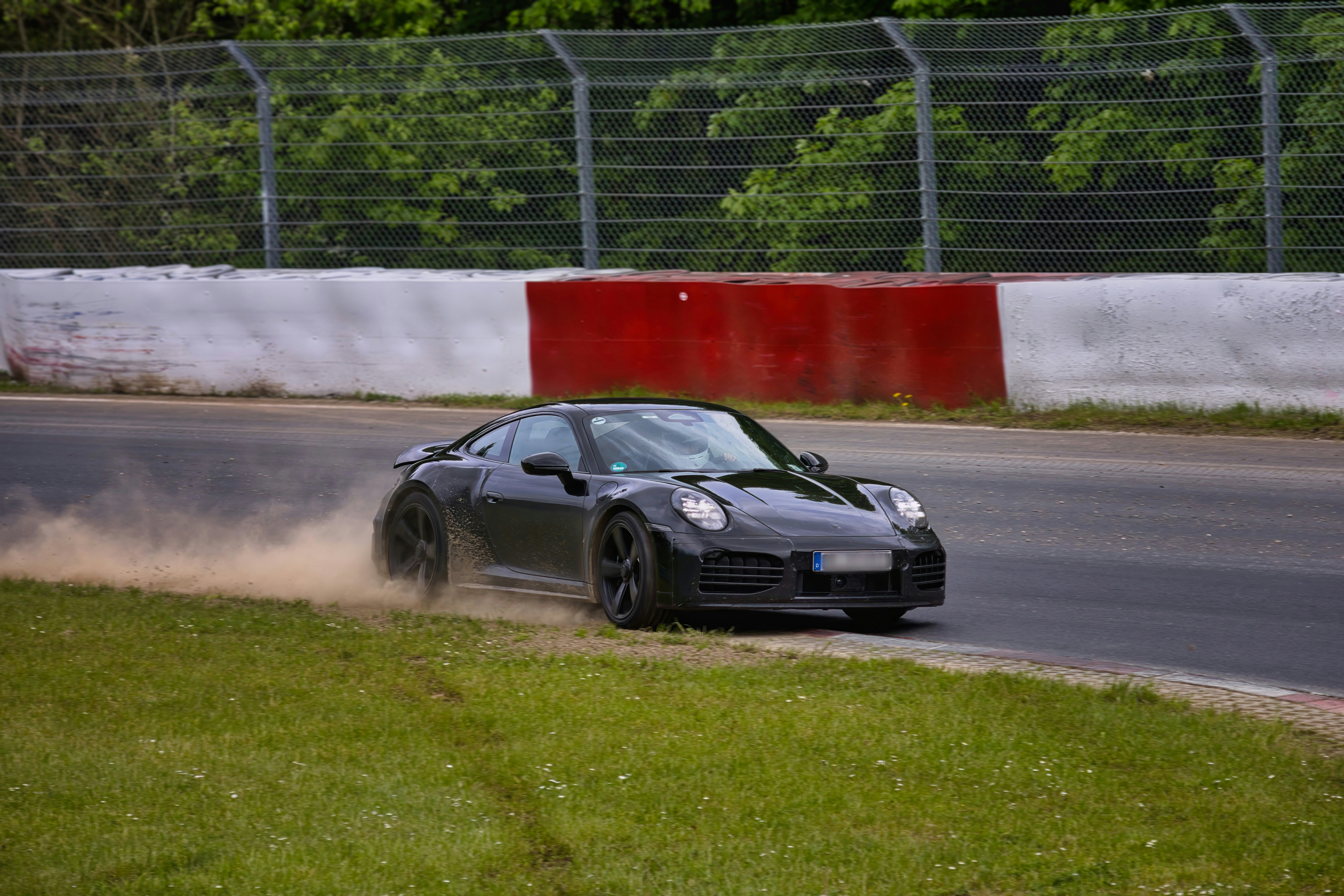 Black sports car kicks up dirt on a race track.