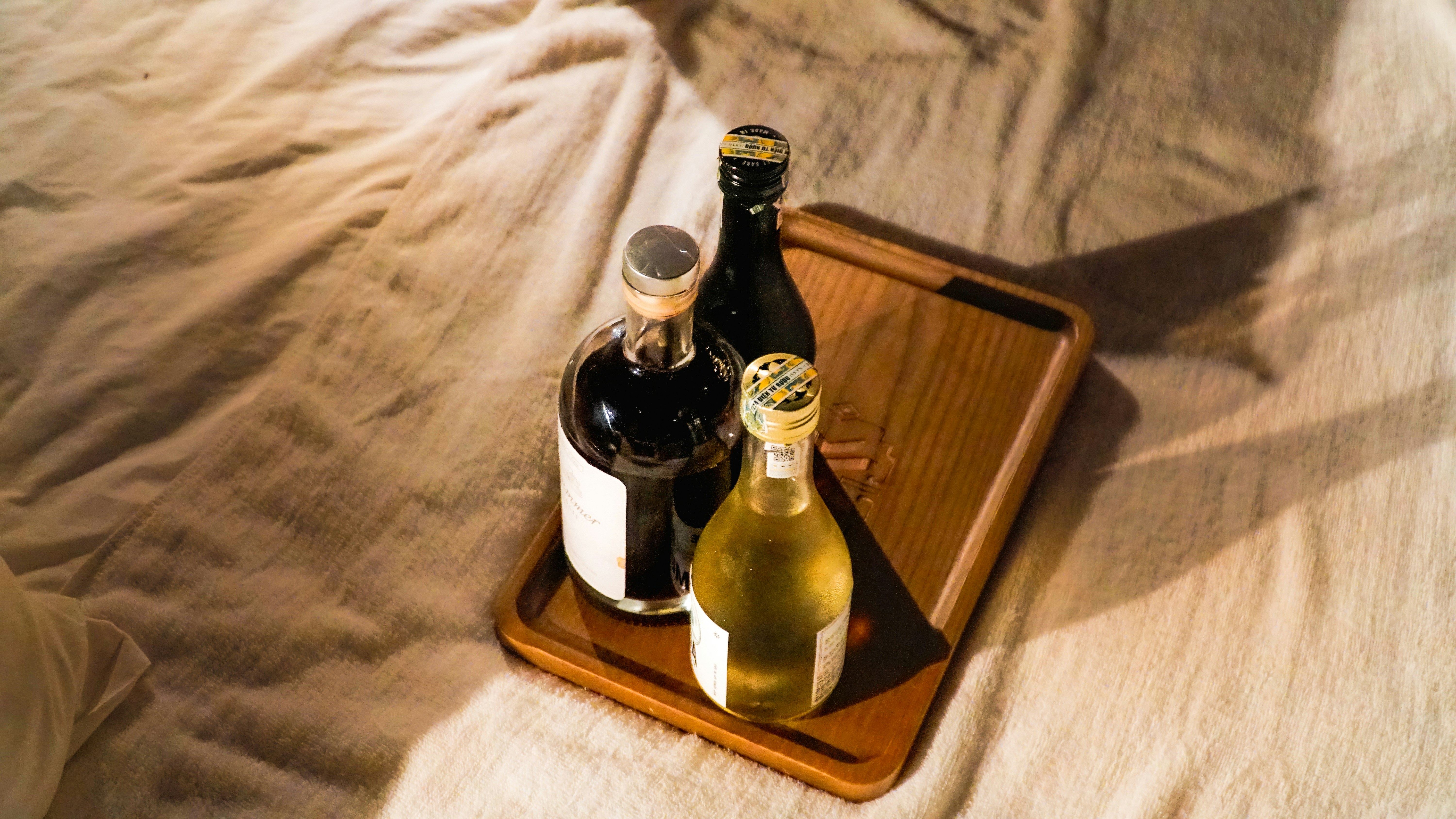 Three bottles on a wooden tray on a rumpled bed.