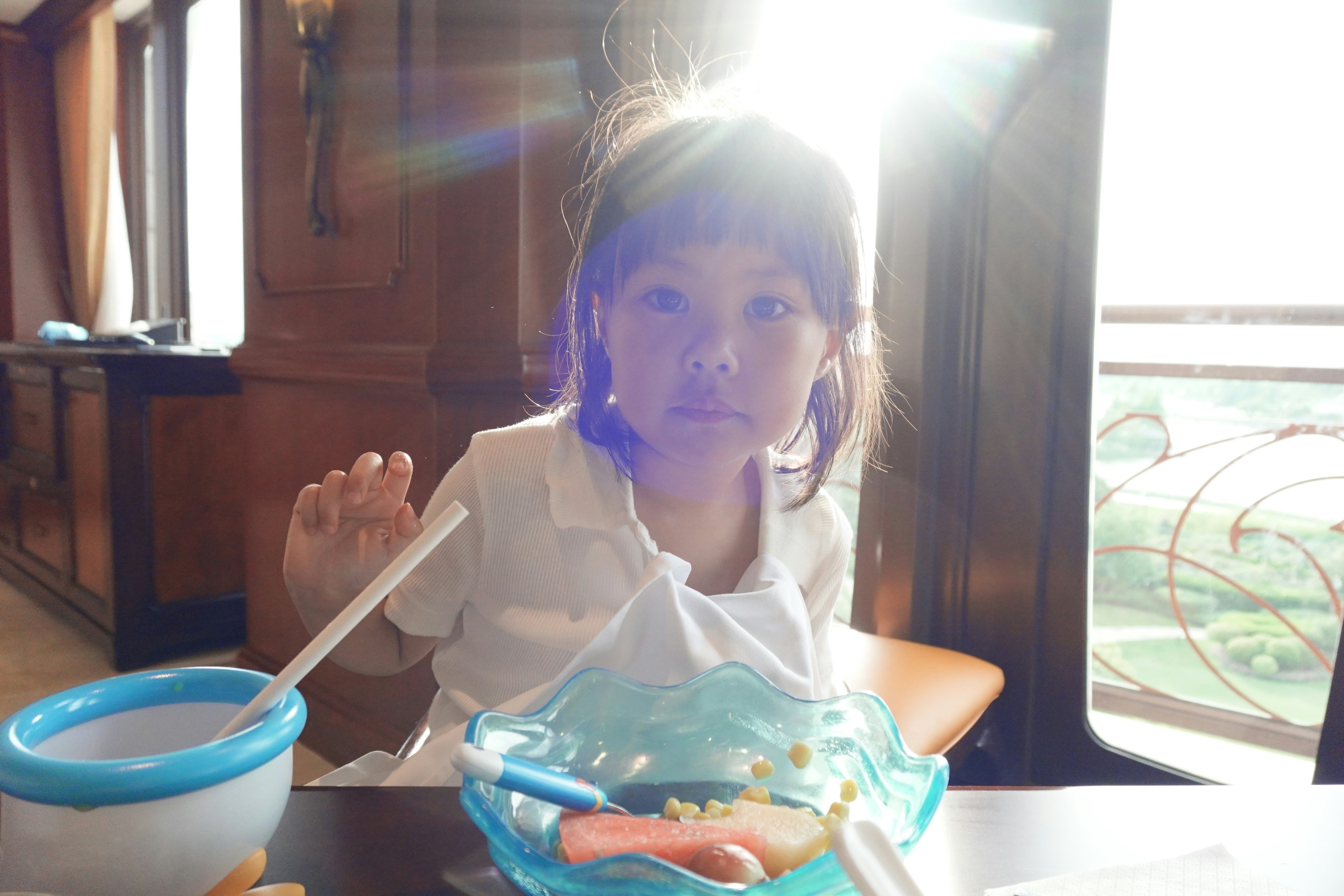 A young girl eating at a table with bright sunlight.