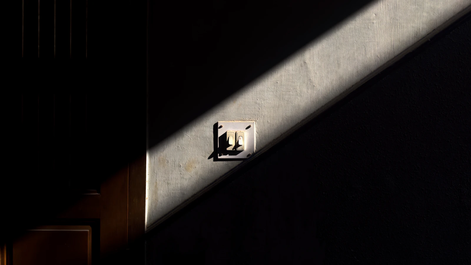 Light switch on a dark wall lit by sunlight