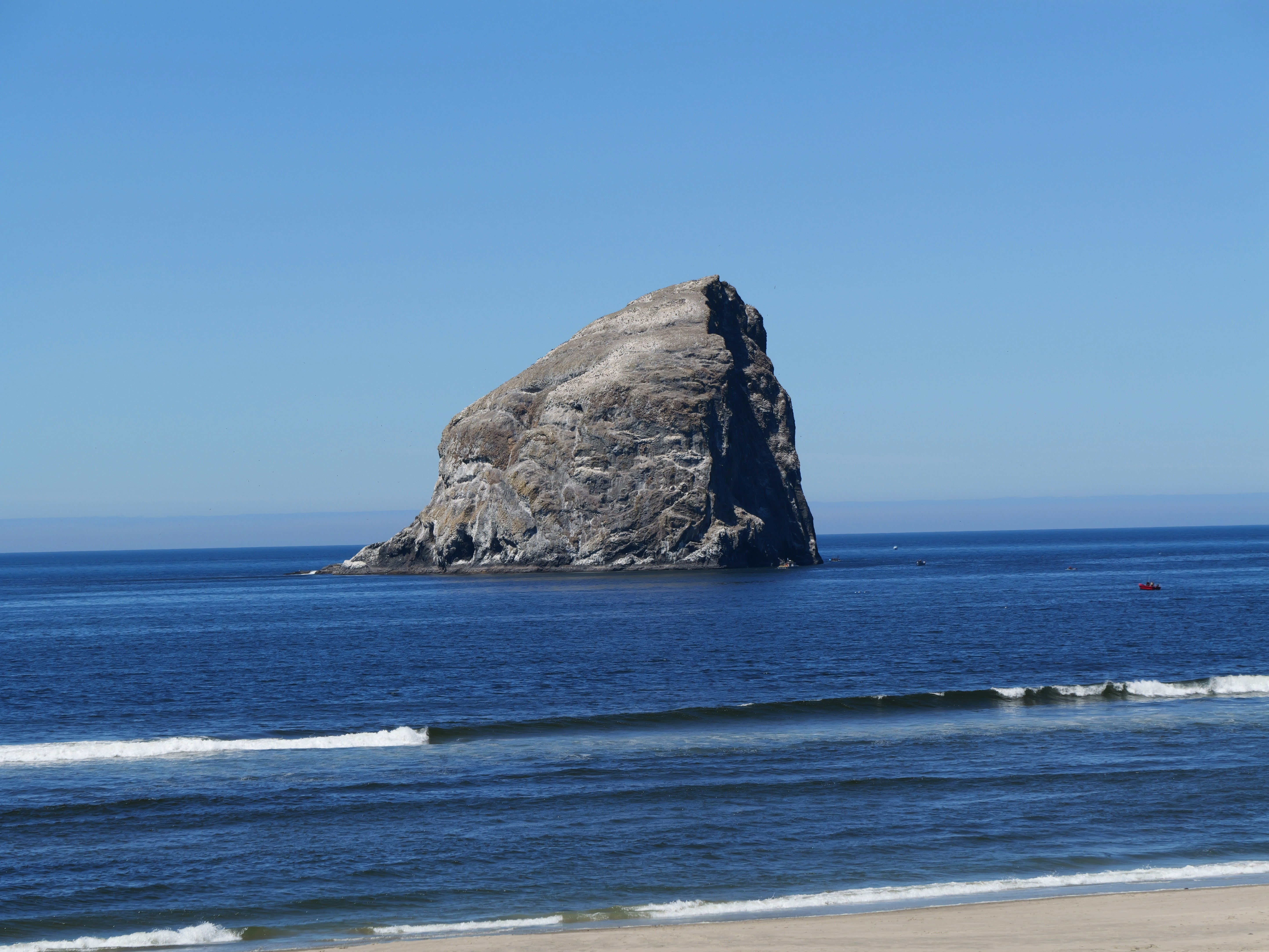 Seastack rock in blue ocean with sandy beach.