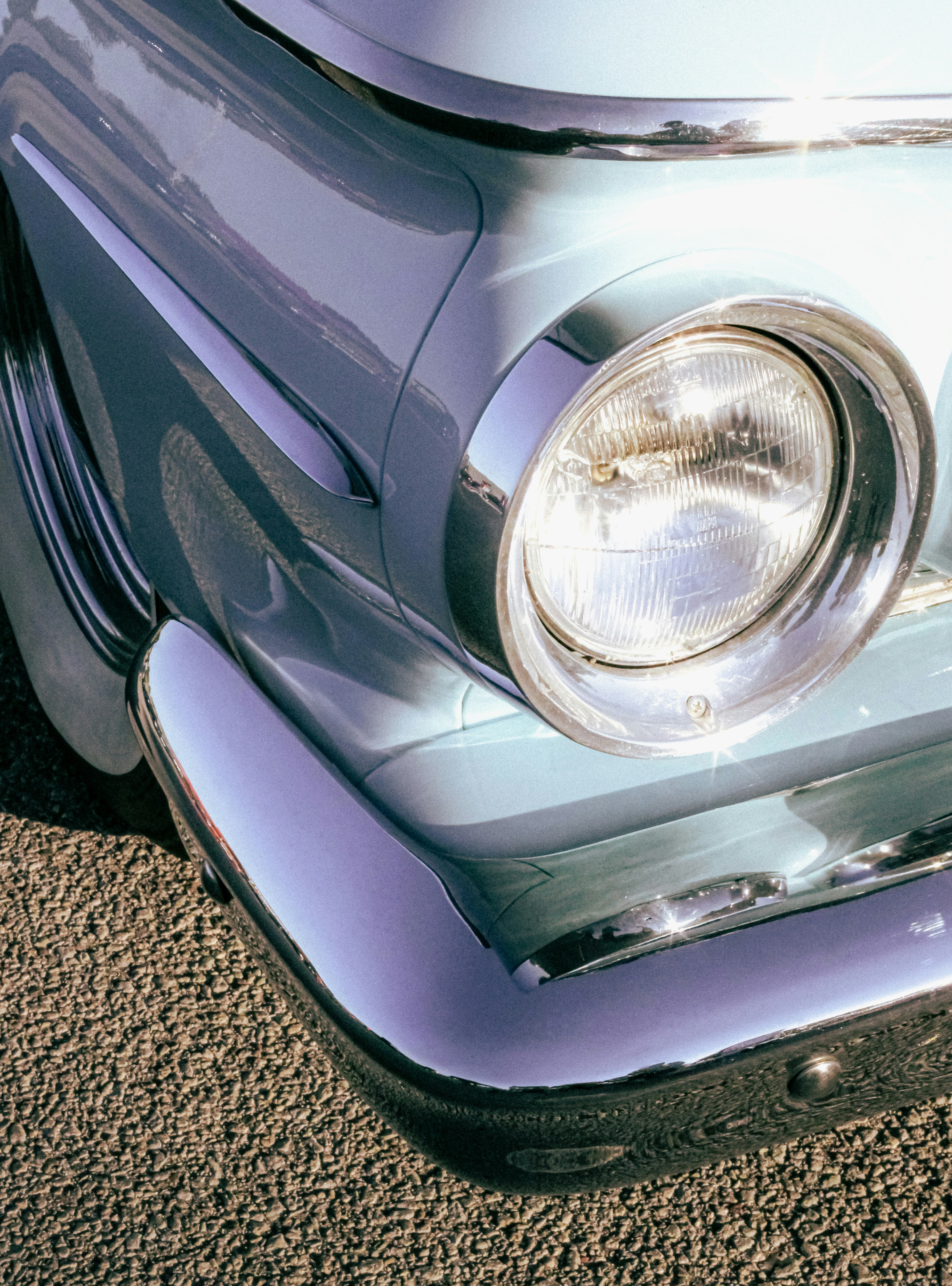 headlight of teal vintage classic car parked in sunlight