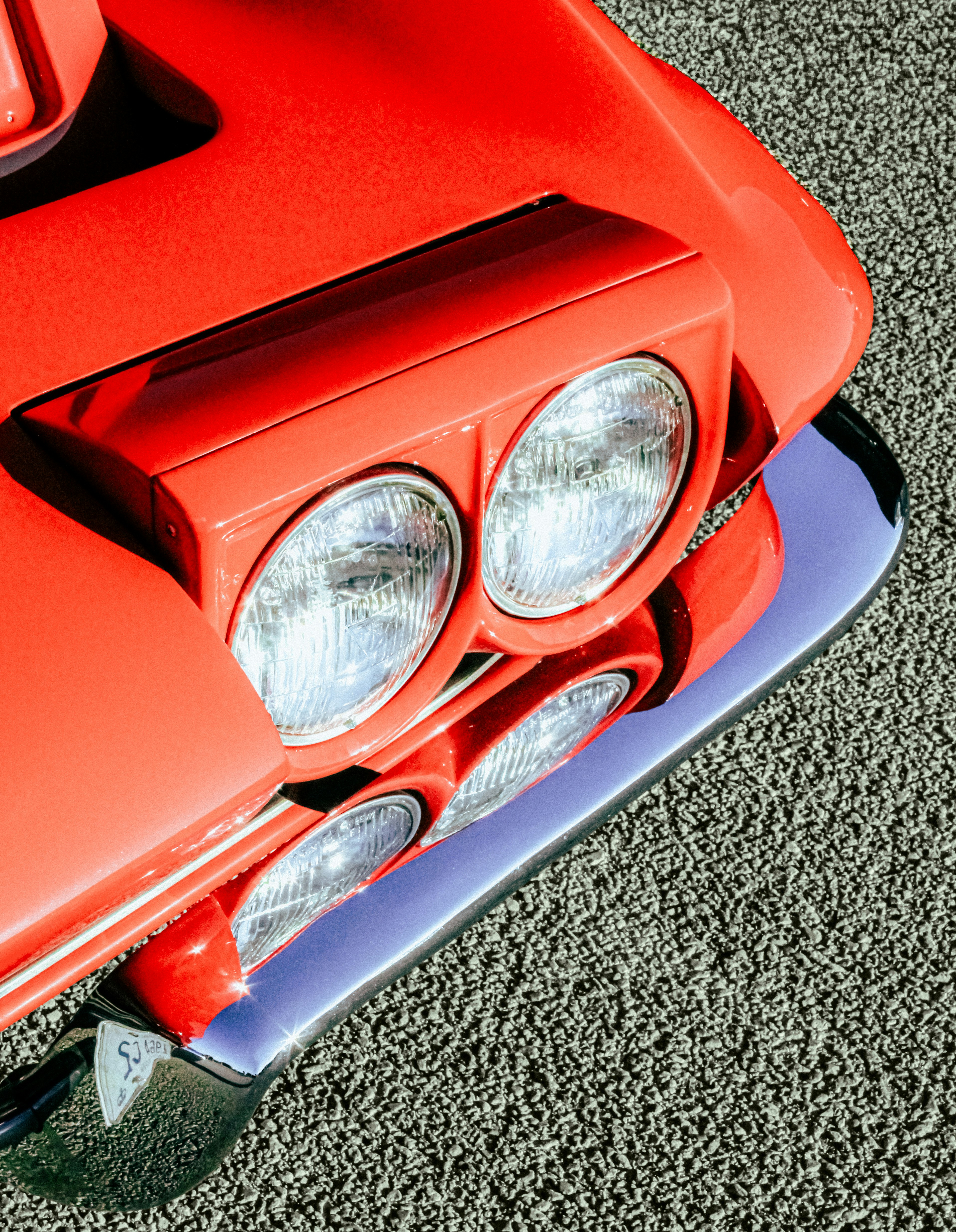 Faróis vermelhos de carro vintage e para-choque cromado sobre chão texturizado.
