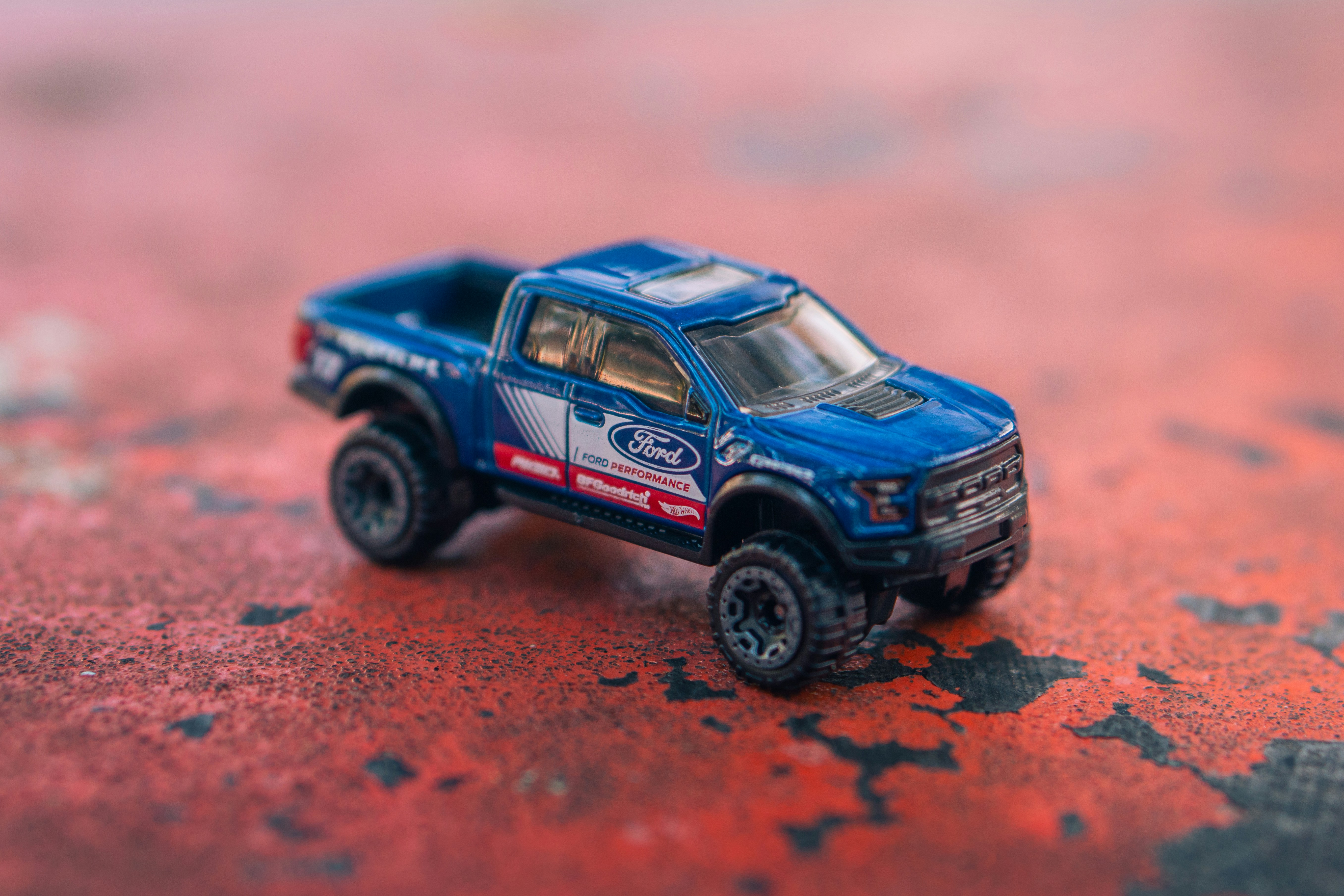 A blue ford raptor toy truck on a red surface.