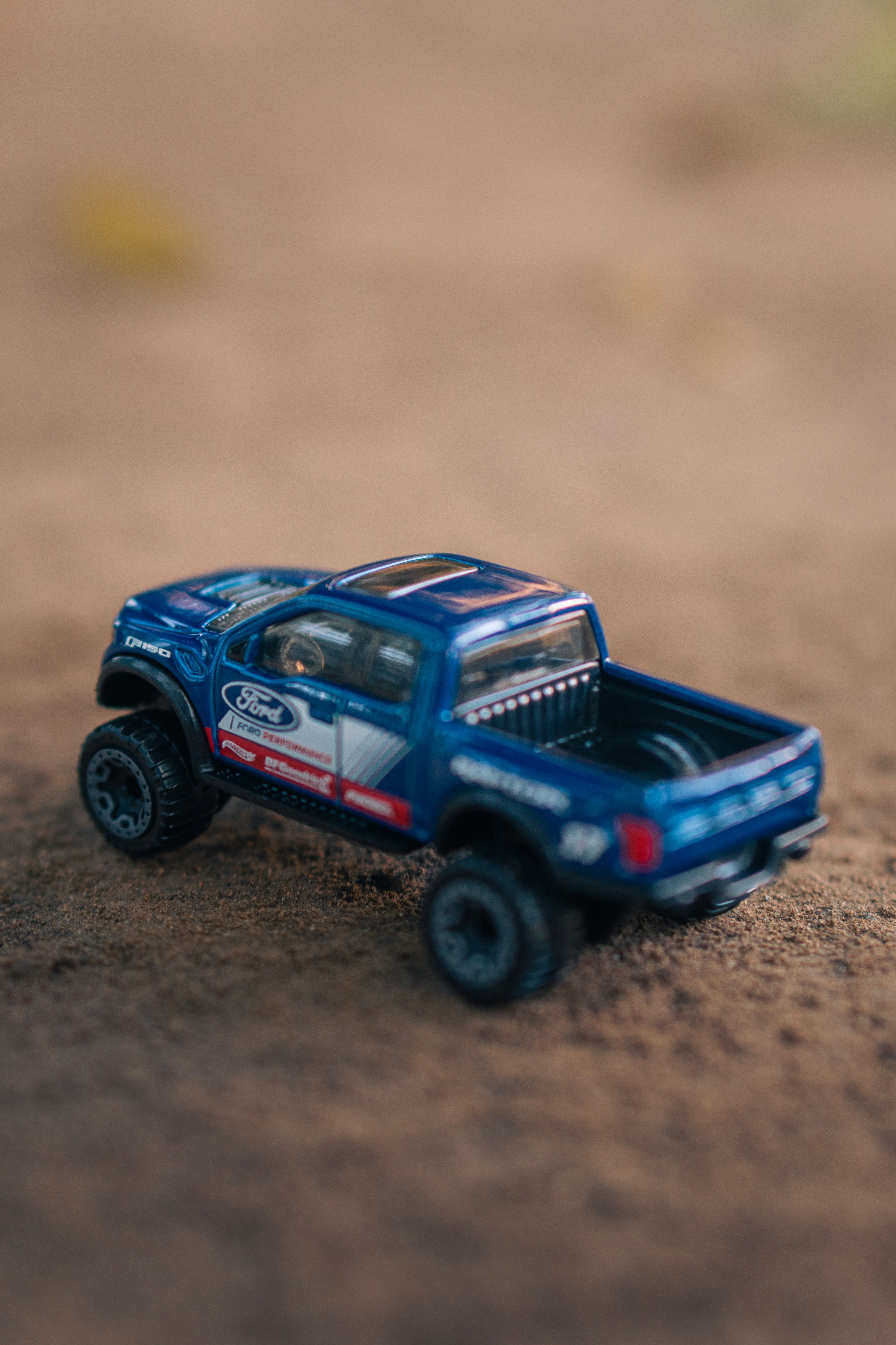 A blue toy ford pickup truck sits on sandy ground.