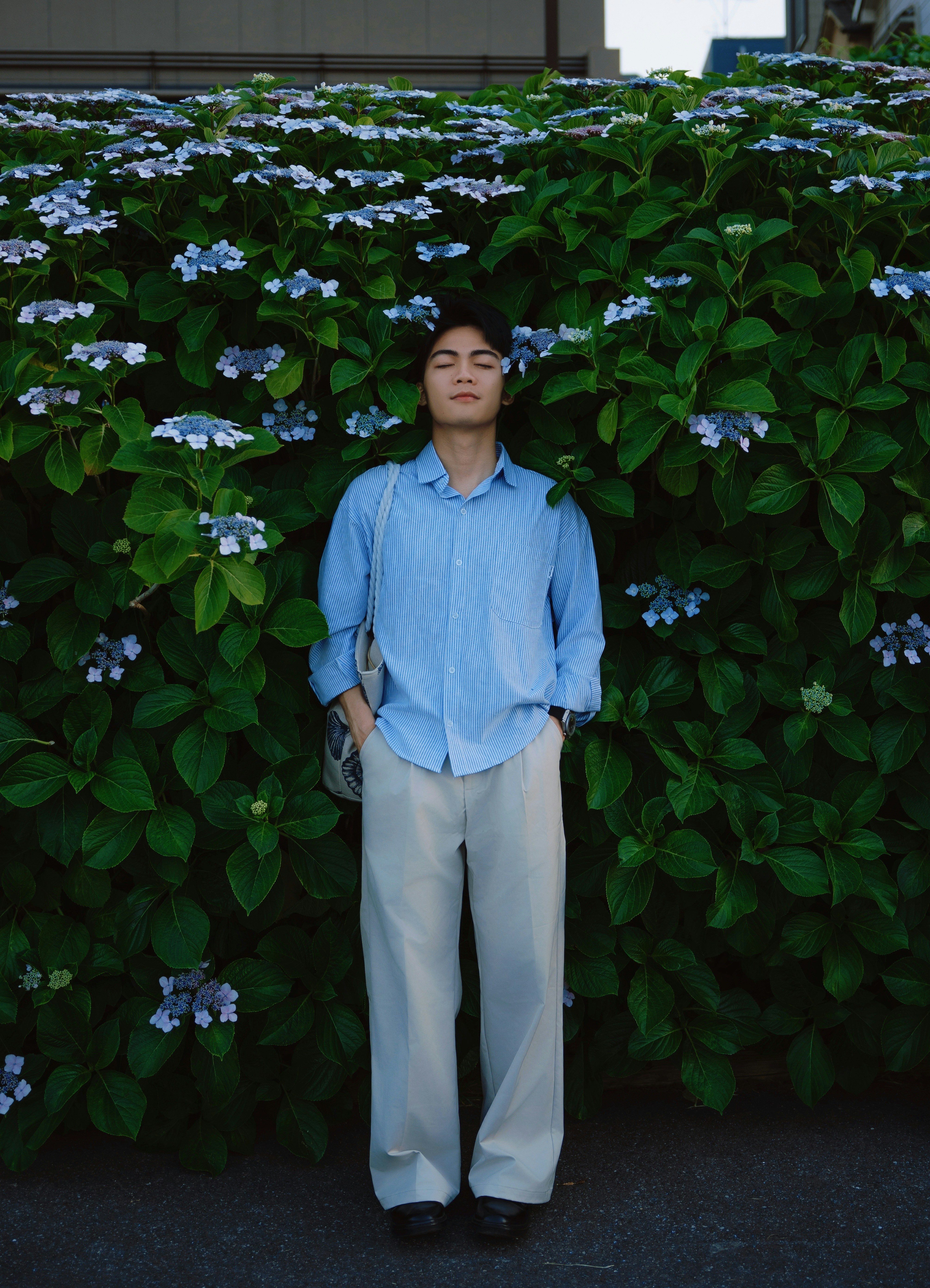 Young man against a green bush with blue flowers.