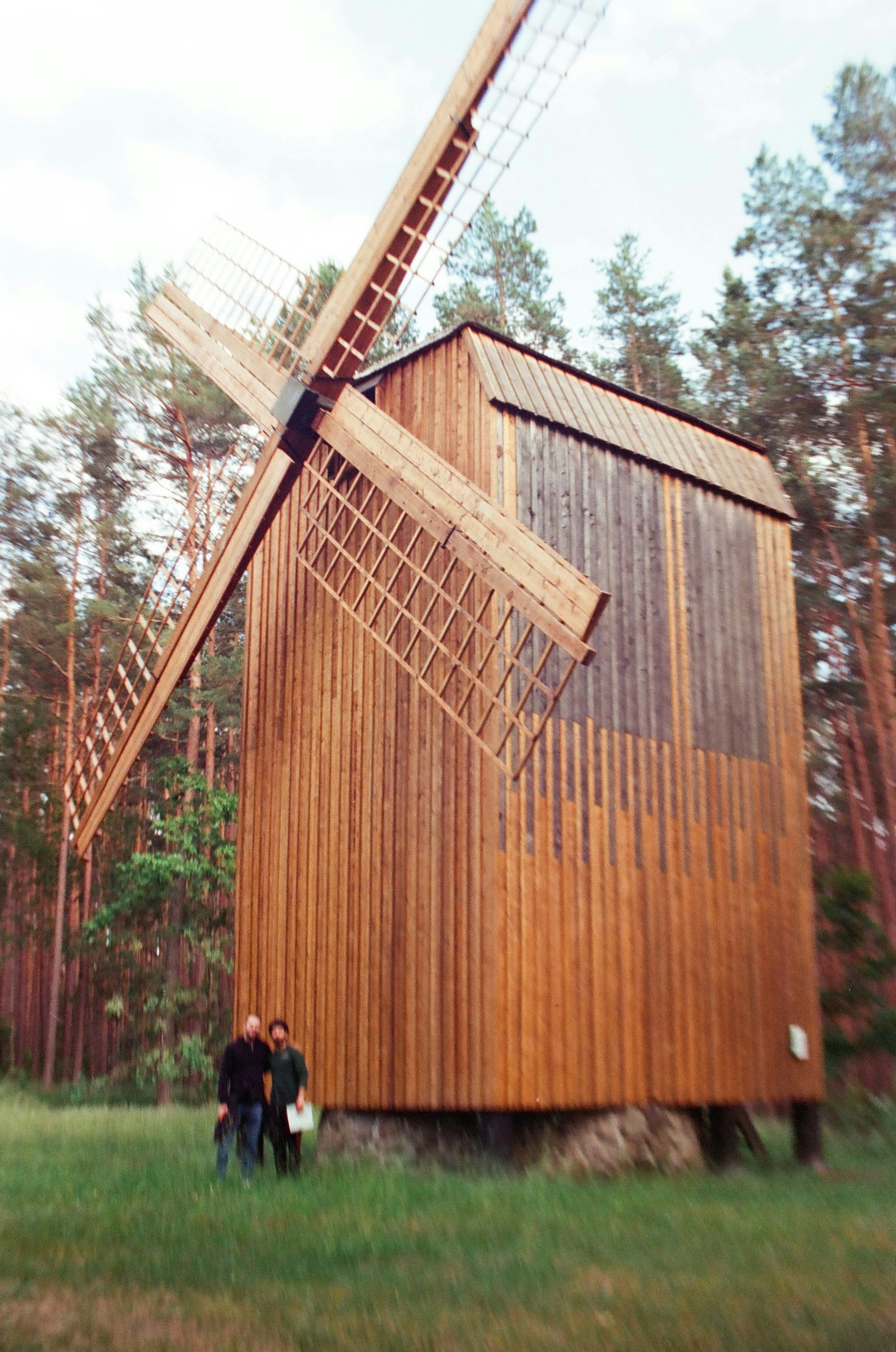 Two individuals next to a traditional wooden windmill