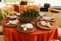 Red table setting with orange flower centerpiece and wooden chairs