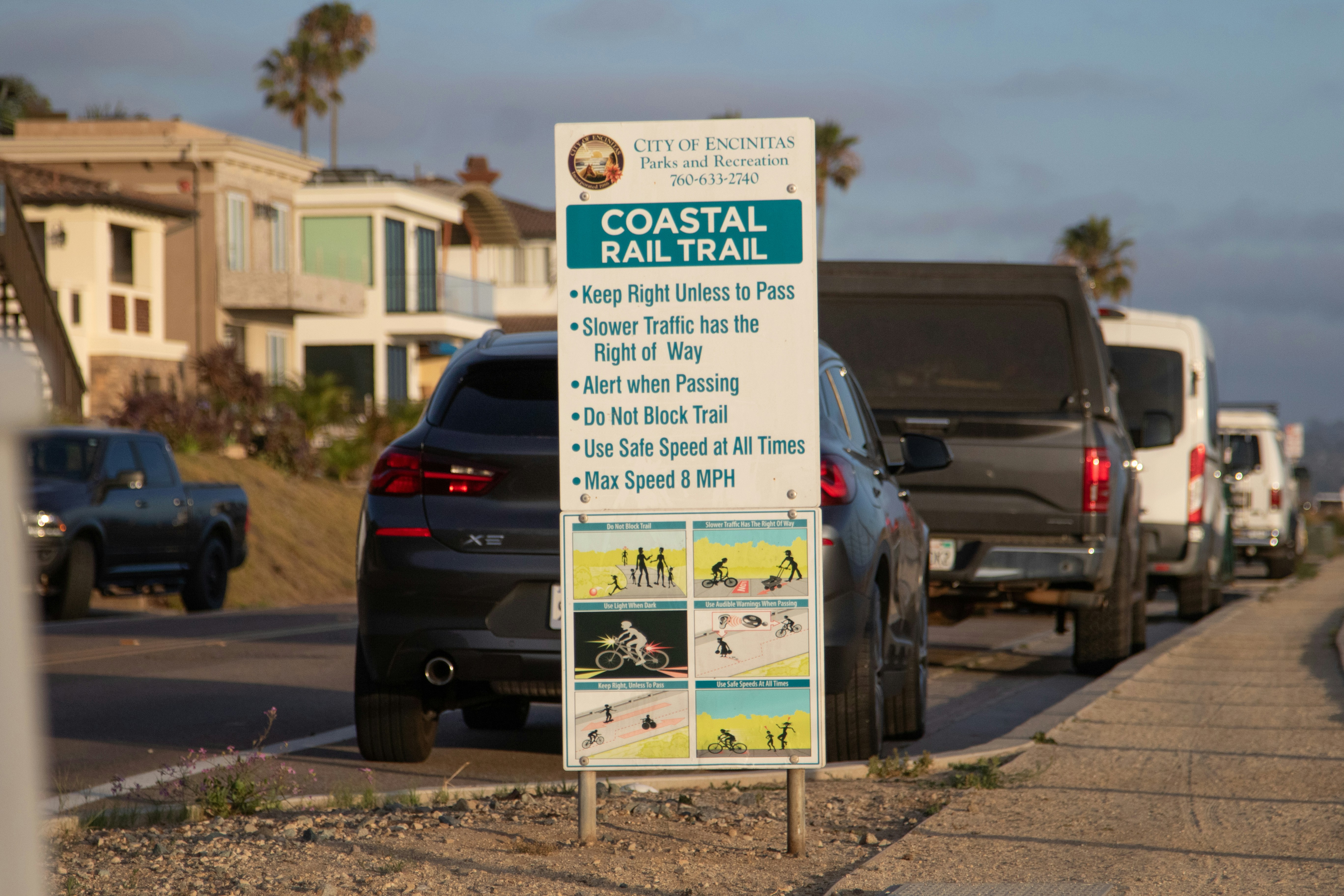 A sign for the coastal rail trail with cars nearby.