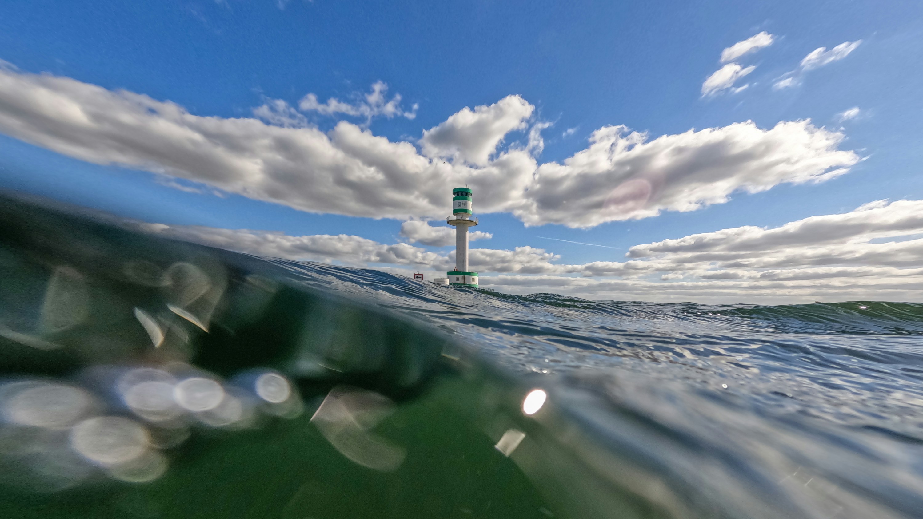 Marine beacon above and below water with cloudy blue sky.