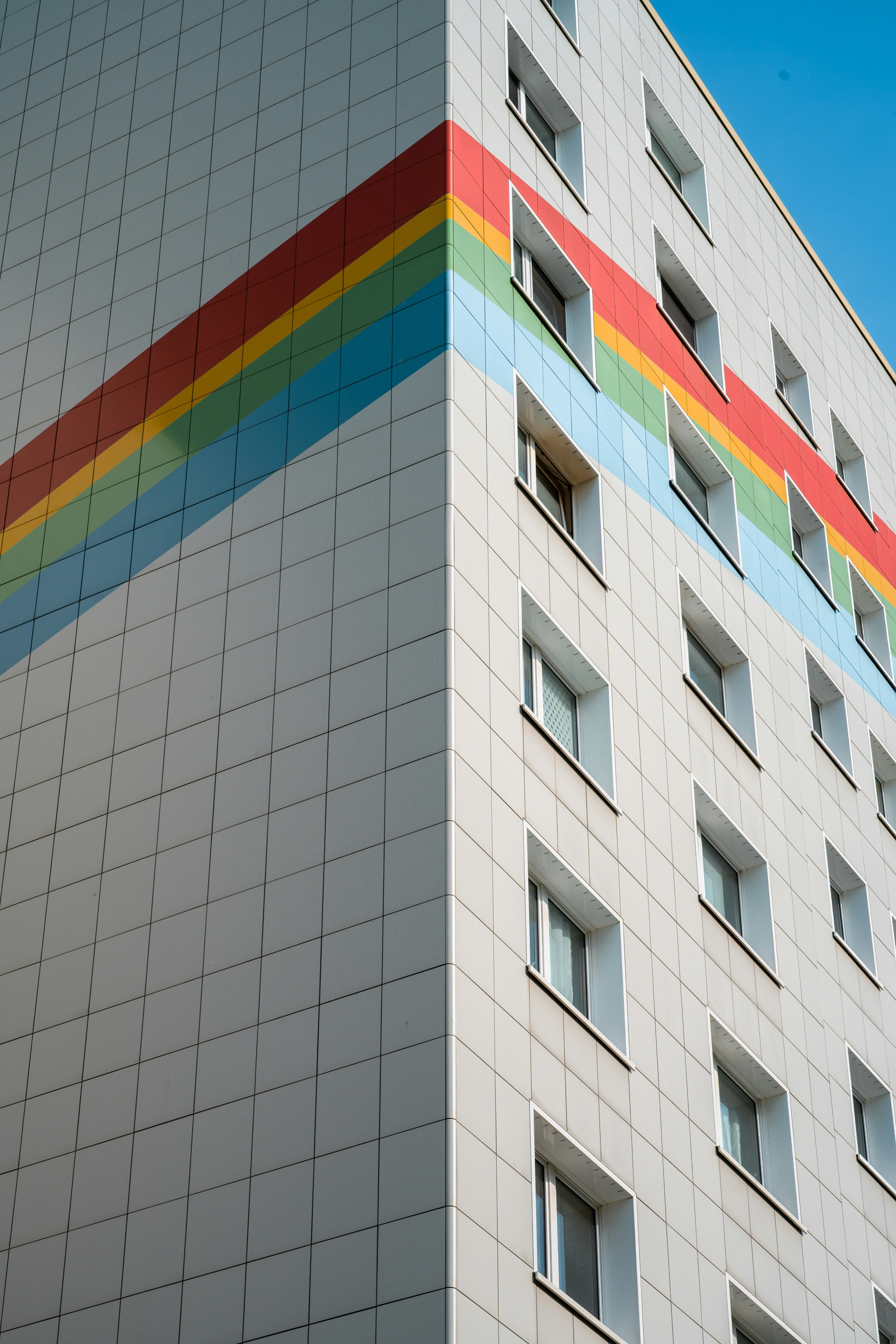 Modern building with a colorful rainbow stripe under blue sky.