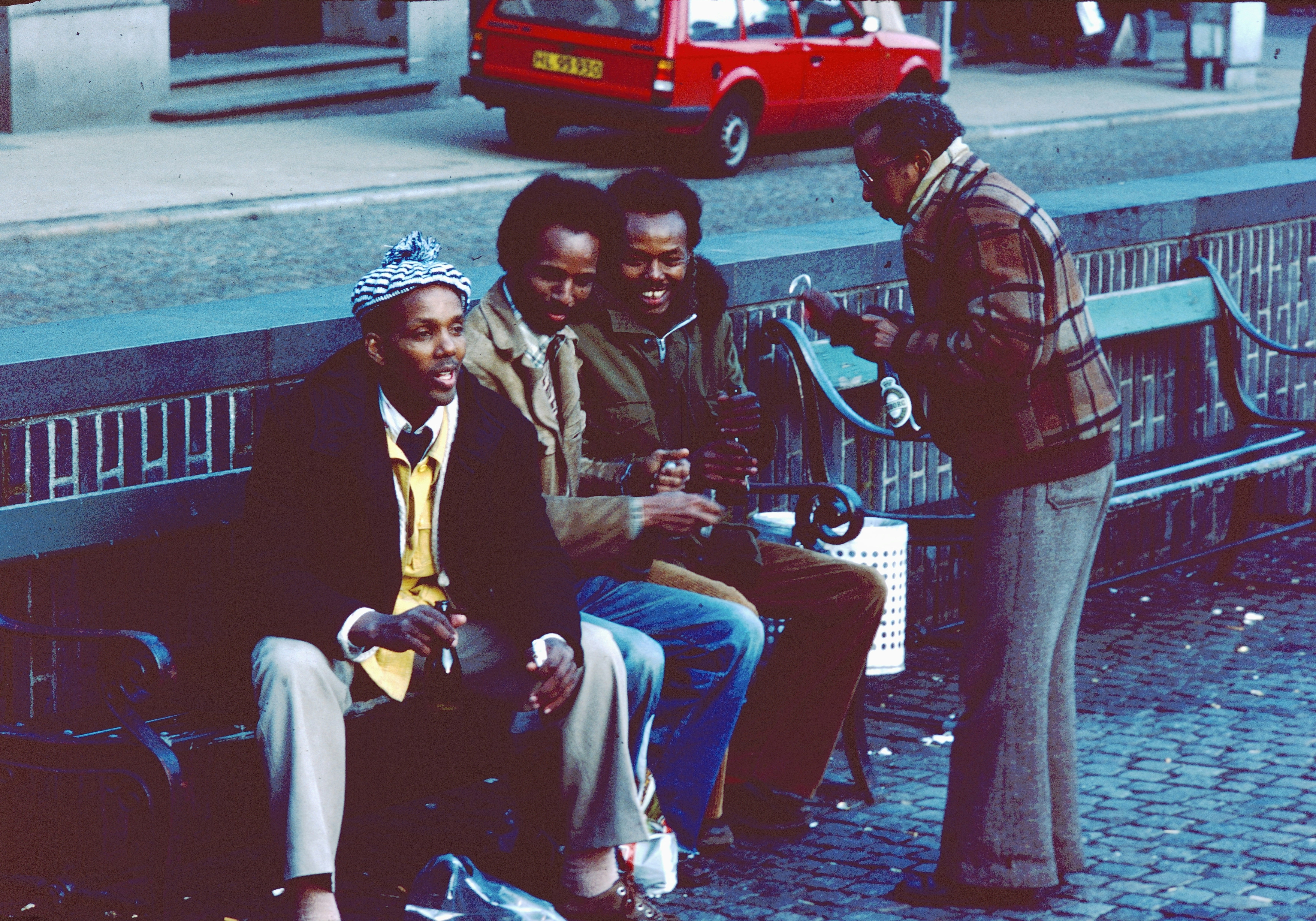 Four men conversing on a city street bench.