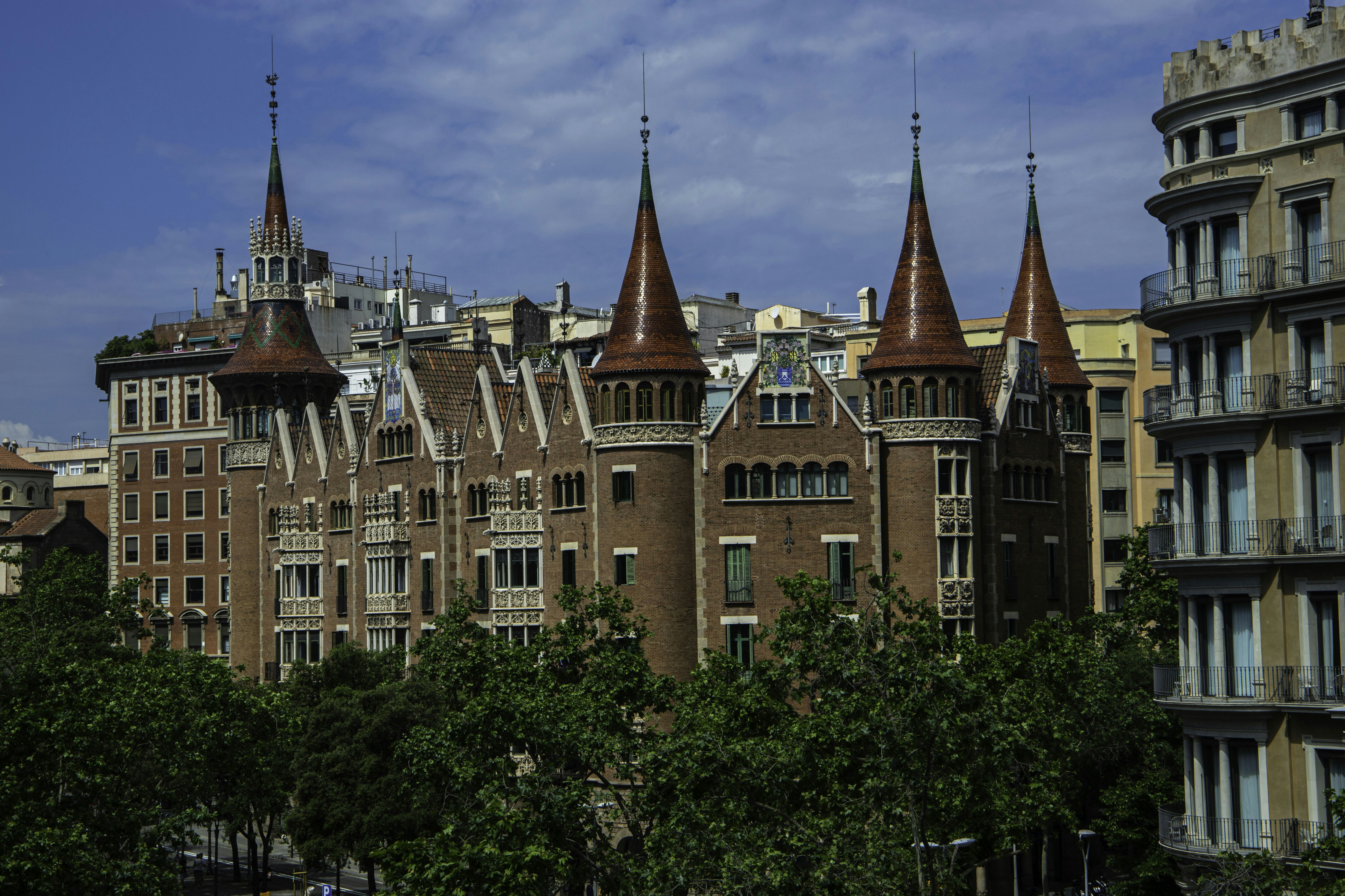 Ornate brick building with red spires surrounded by city trees.
