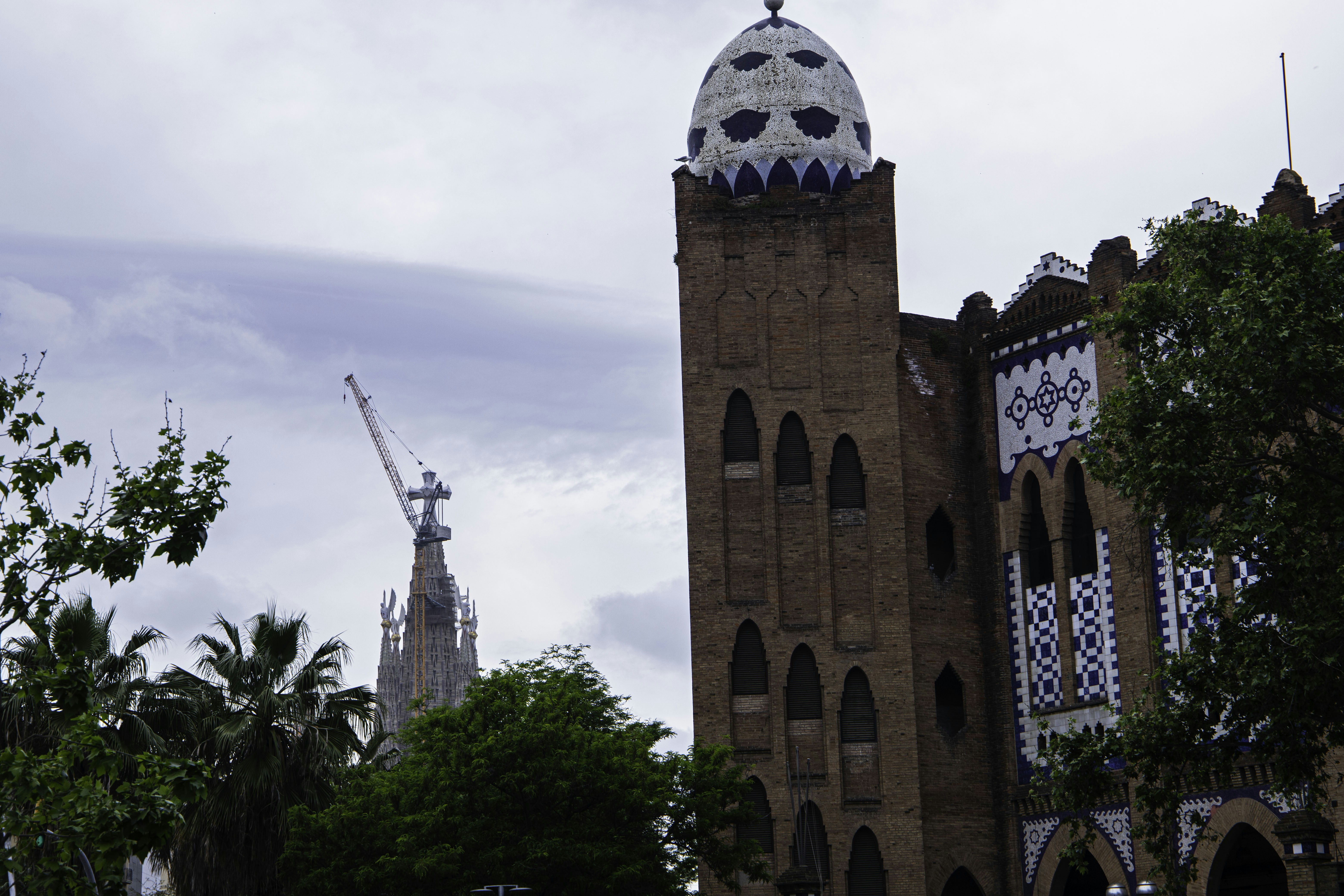 Historic brick building with tiled dome and distant sagrada familia.
