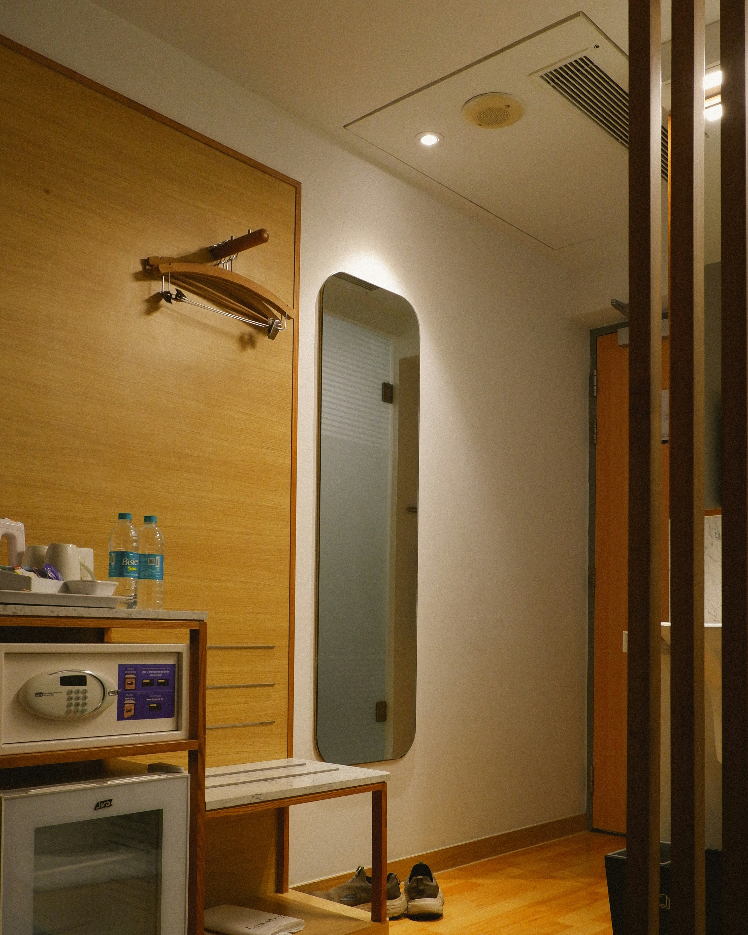 Pintu masuk kamar hotel modern dengan aksen kayu dan cermin panjang penuh.