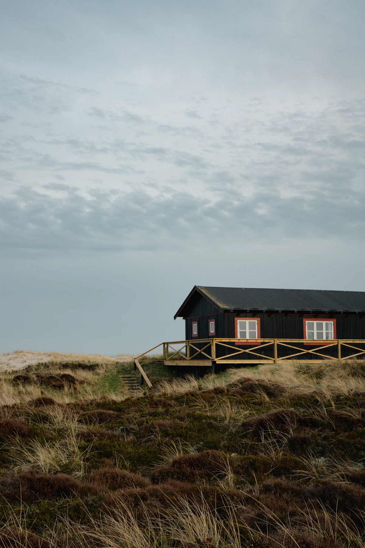 Mørkt træbeklædt sommerhus i et åbent klitlandskab
