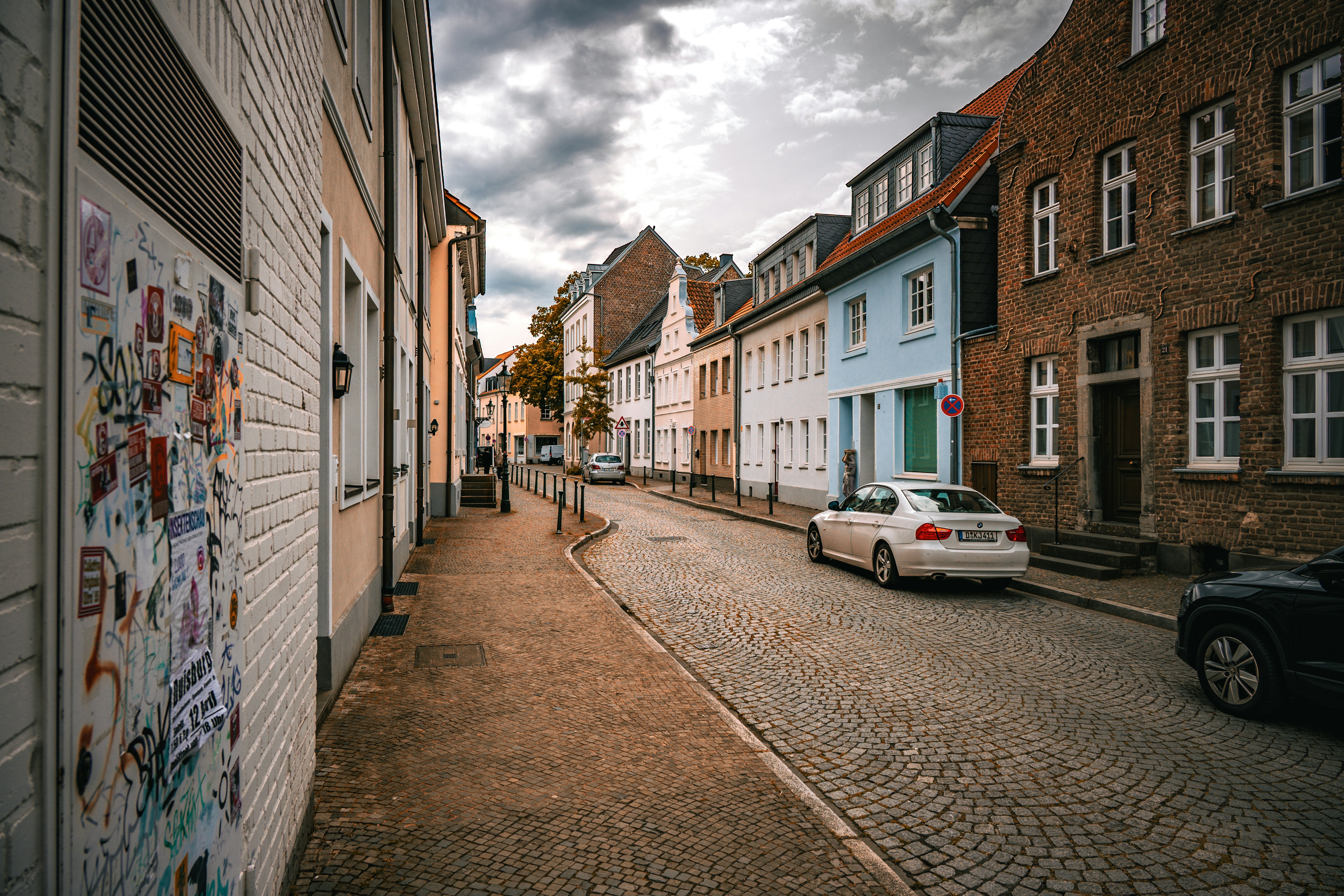 Narrow cobblestone street with colorful buildings under cloudy sky.