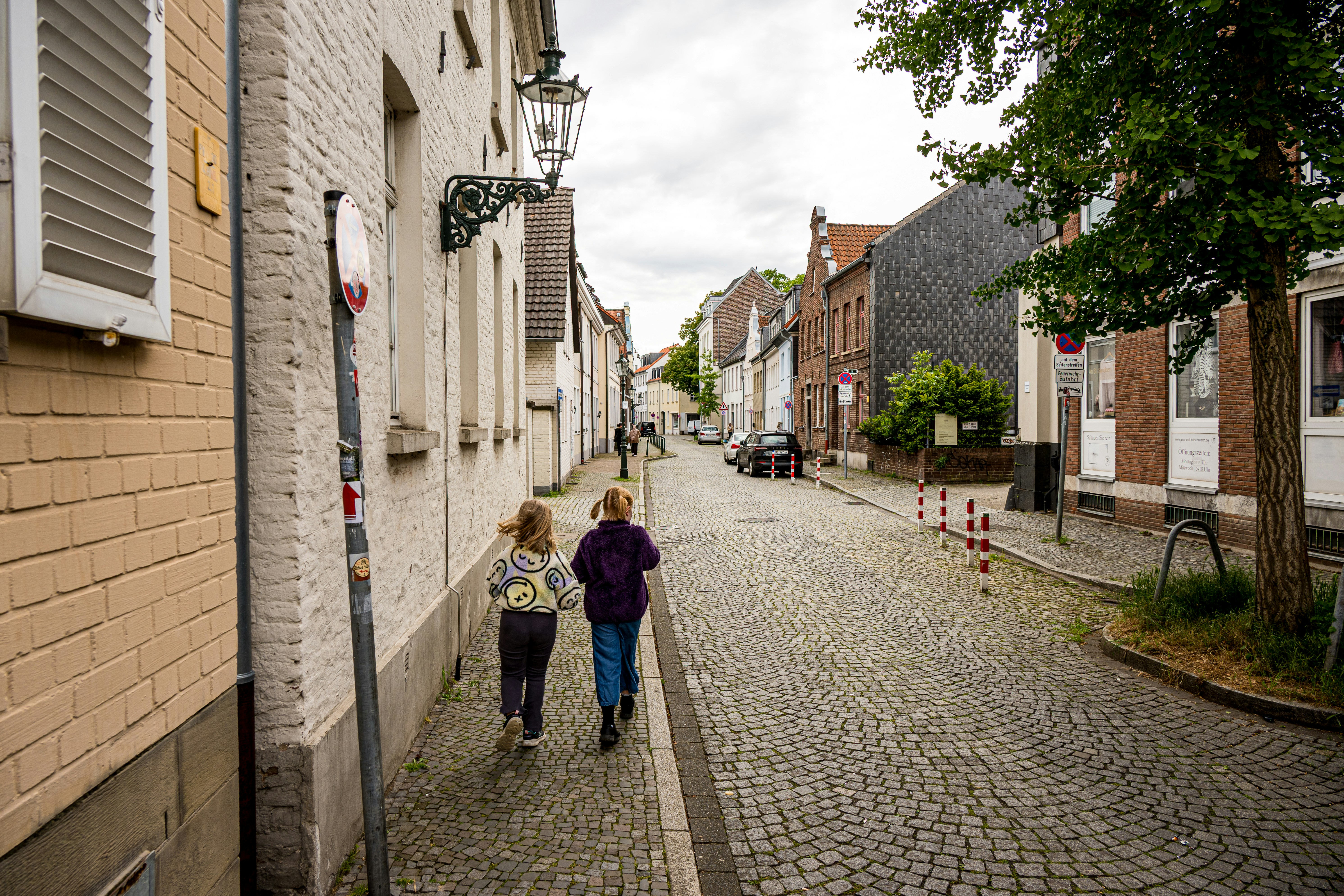 Two children walk down a cobblestone street between old buildings.