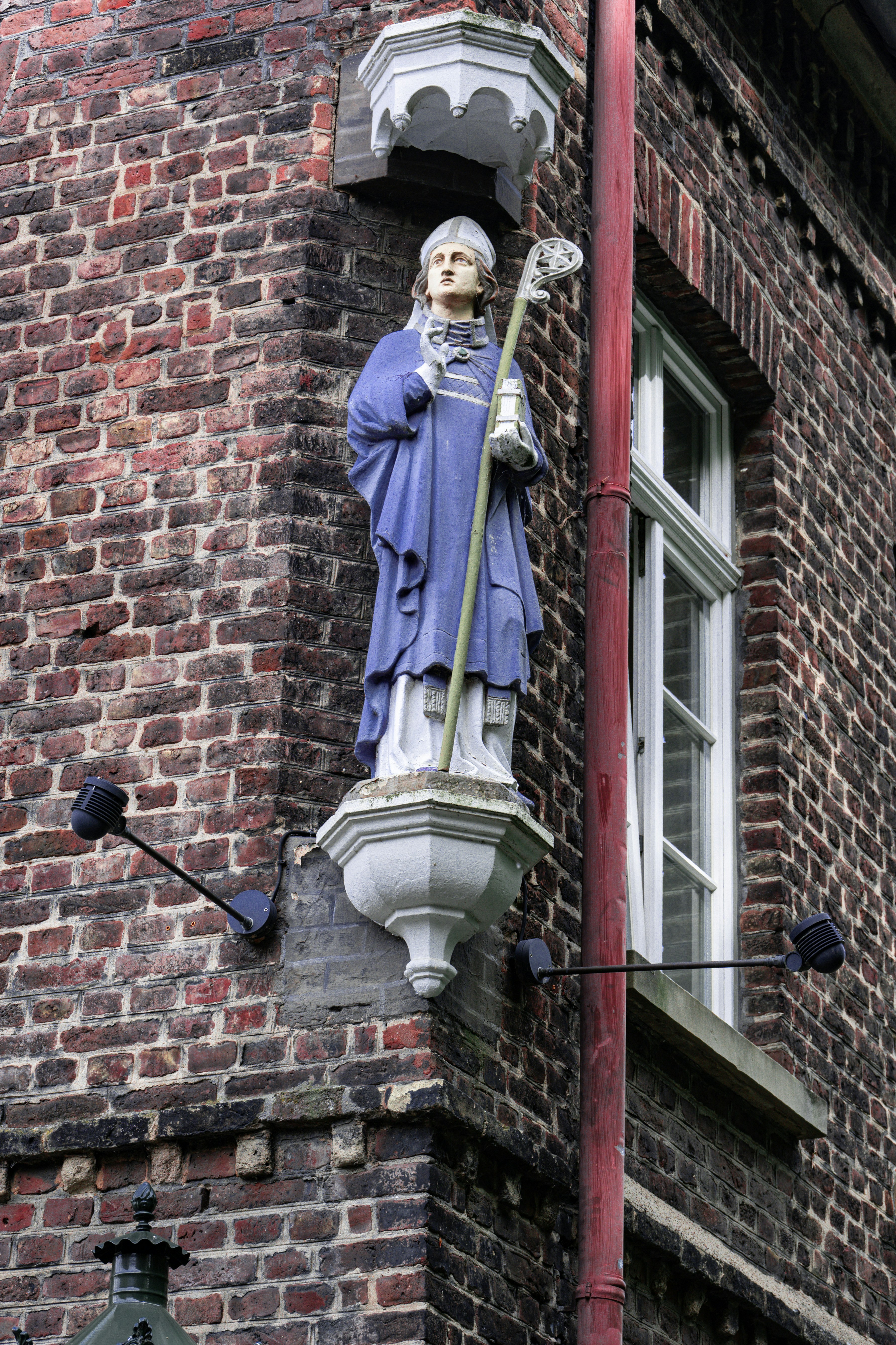 Blue statue of a bishop on a historic brick building.