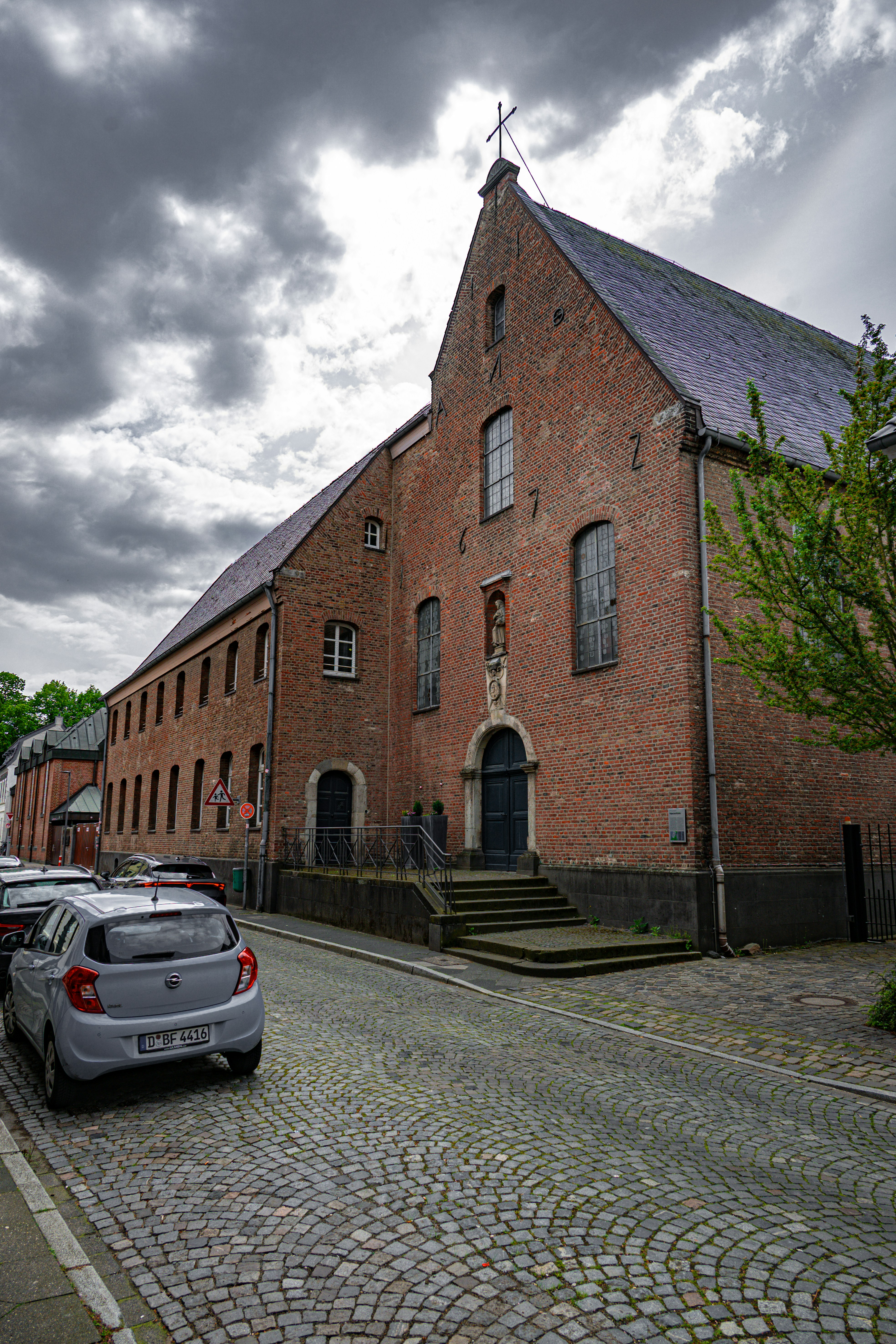 Historic brick building on a cobblestone street under cloudy sky.