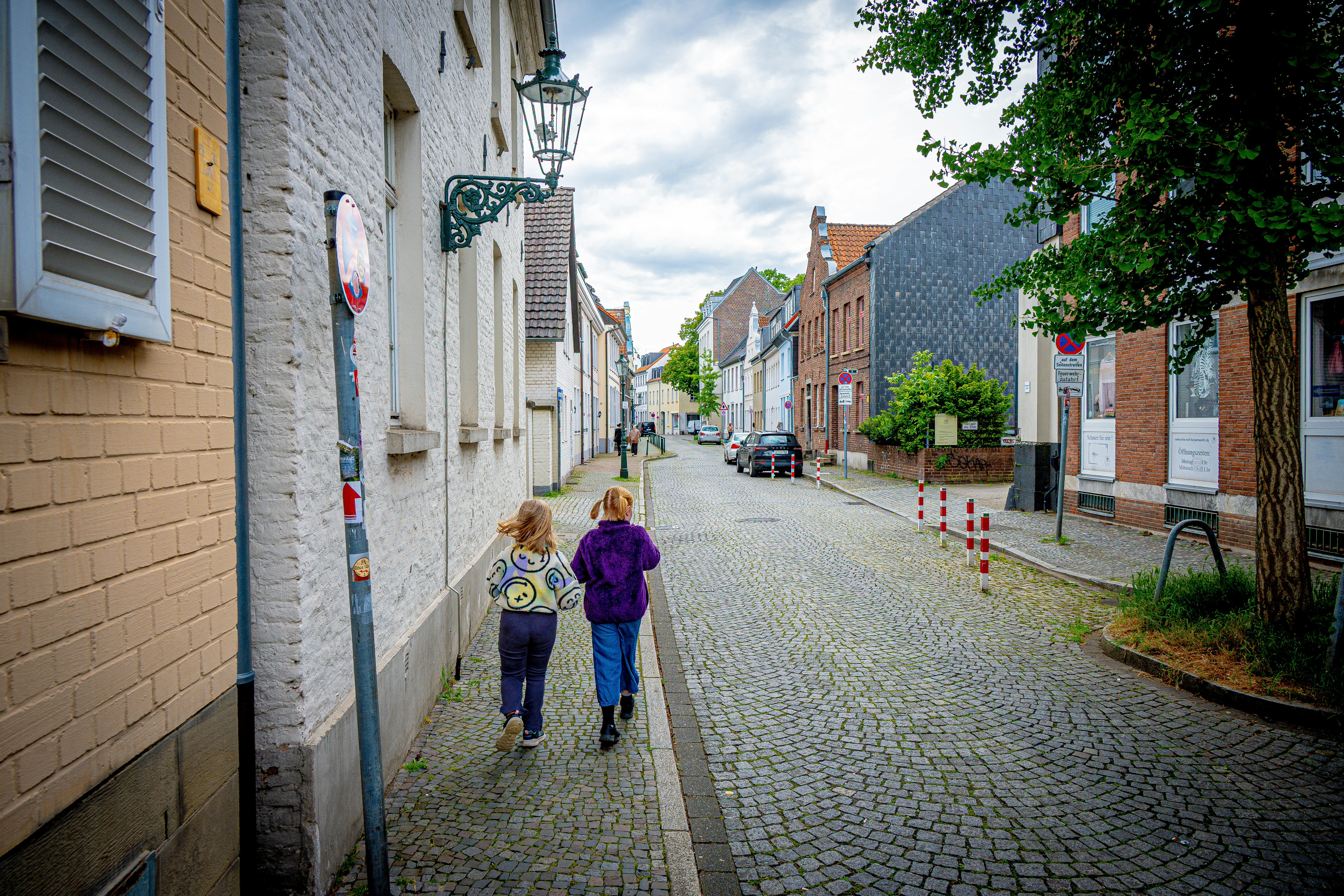 Two people walk down a cobblestone street with old buildings.
