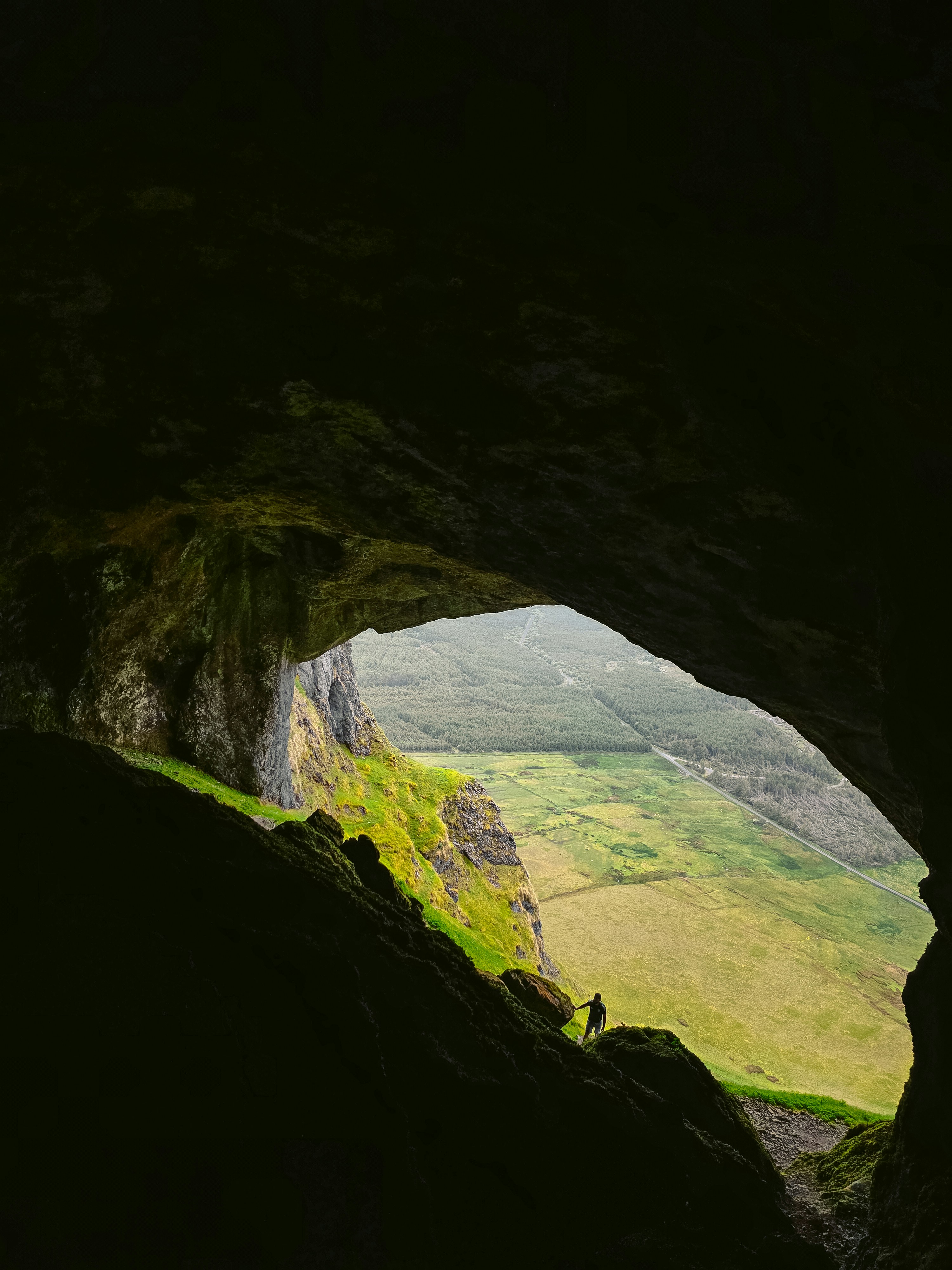 Person si trova all'ingresso della grotta che si affaccia su una valle verde.