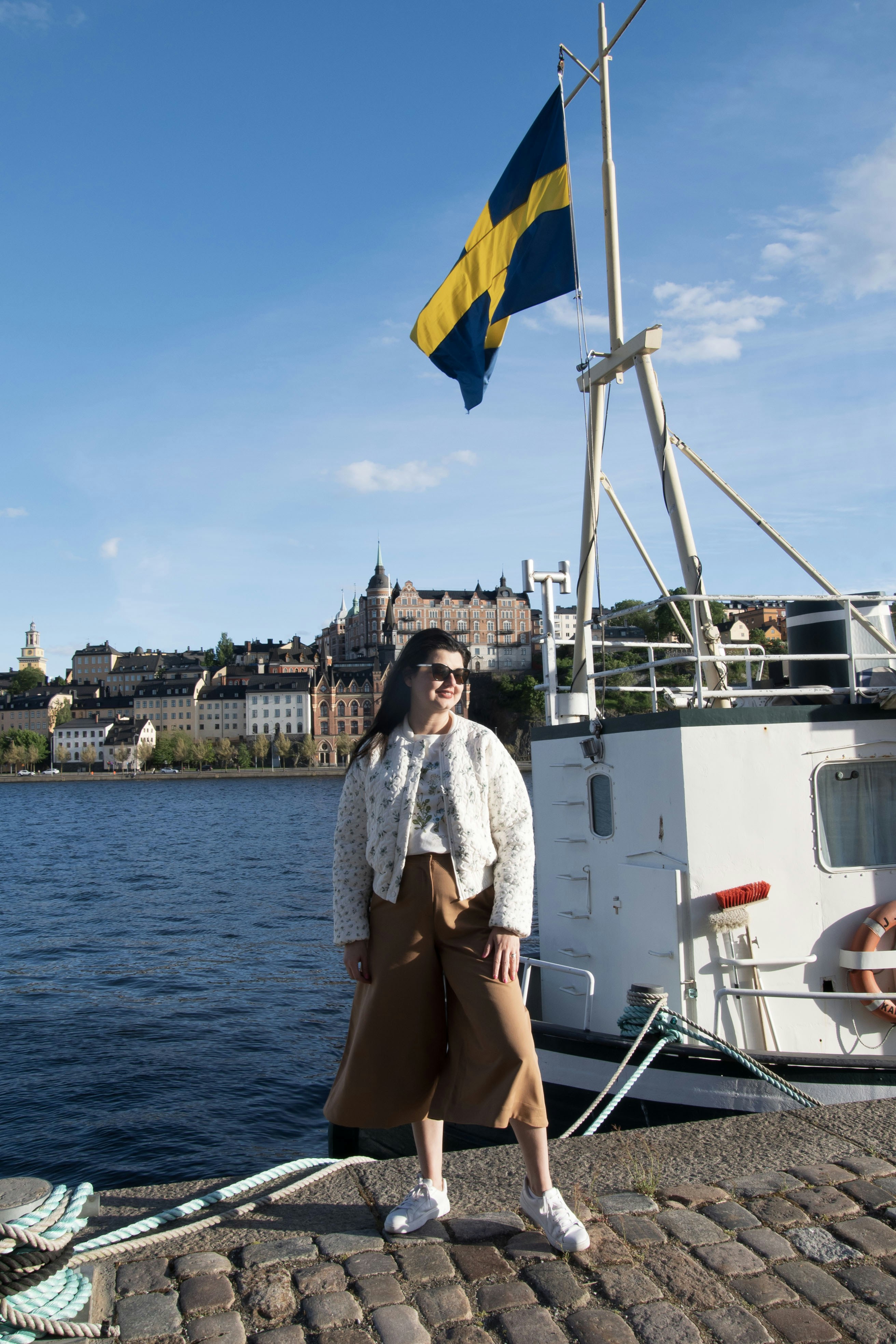 スウェーデンの旗を掲げ、遠くの街景を望む船に乗る女性。