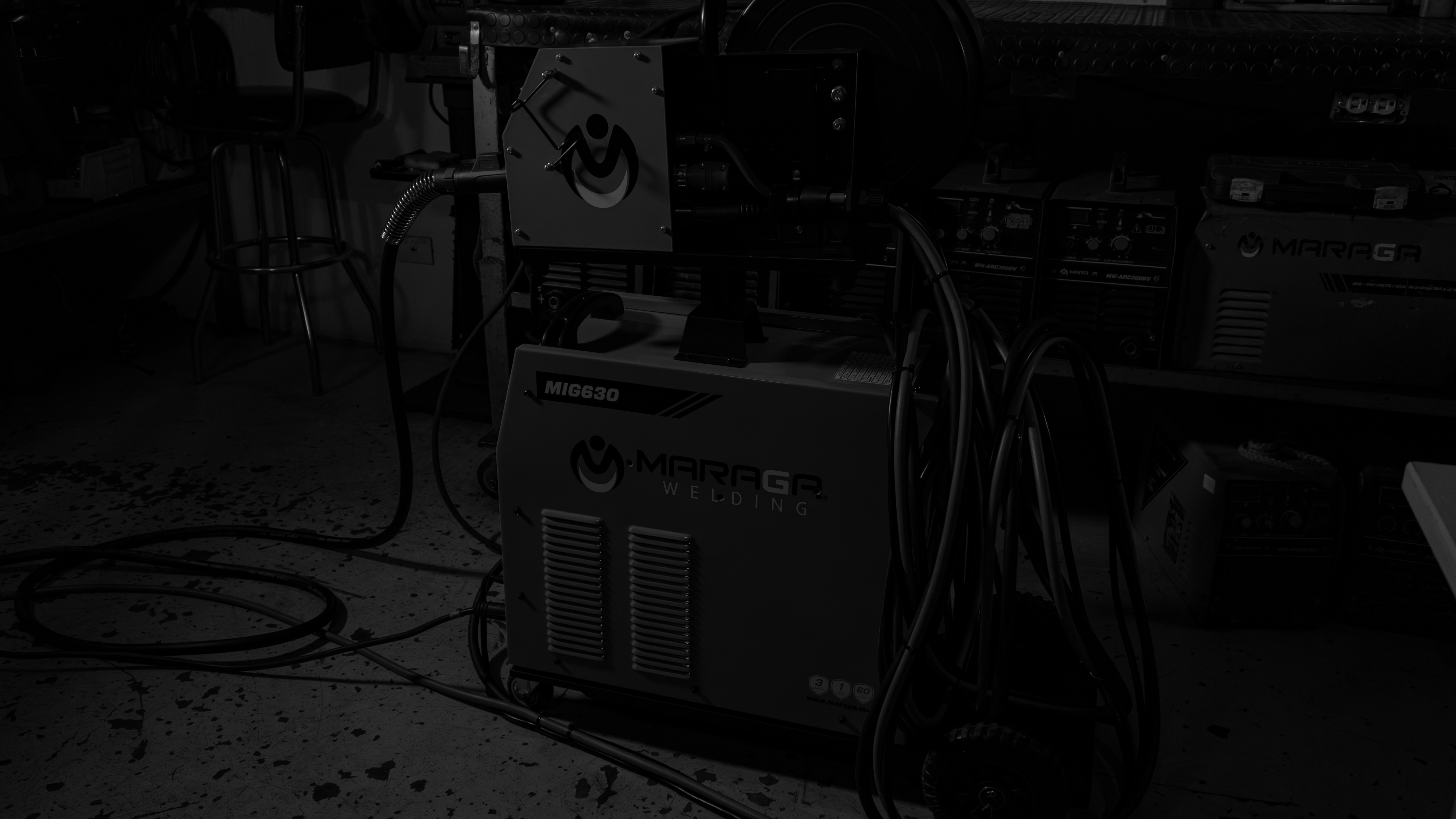 Welding machine with cables in a dark, industrial setting.