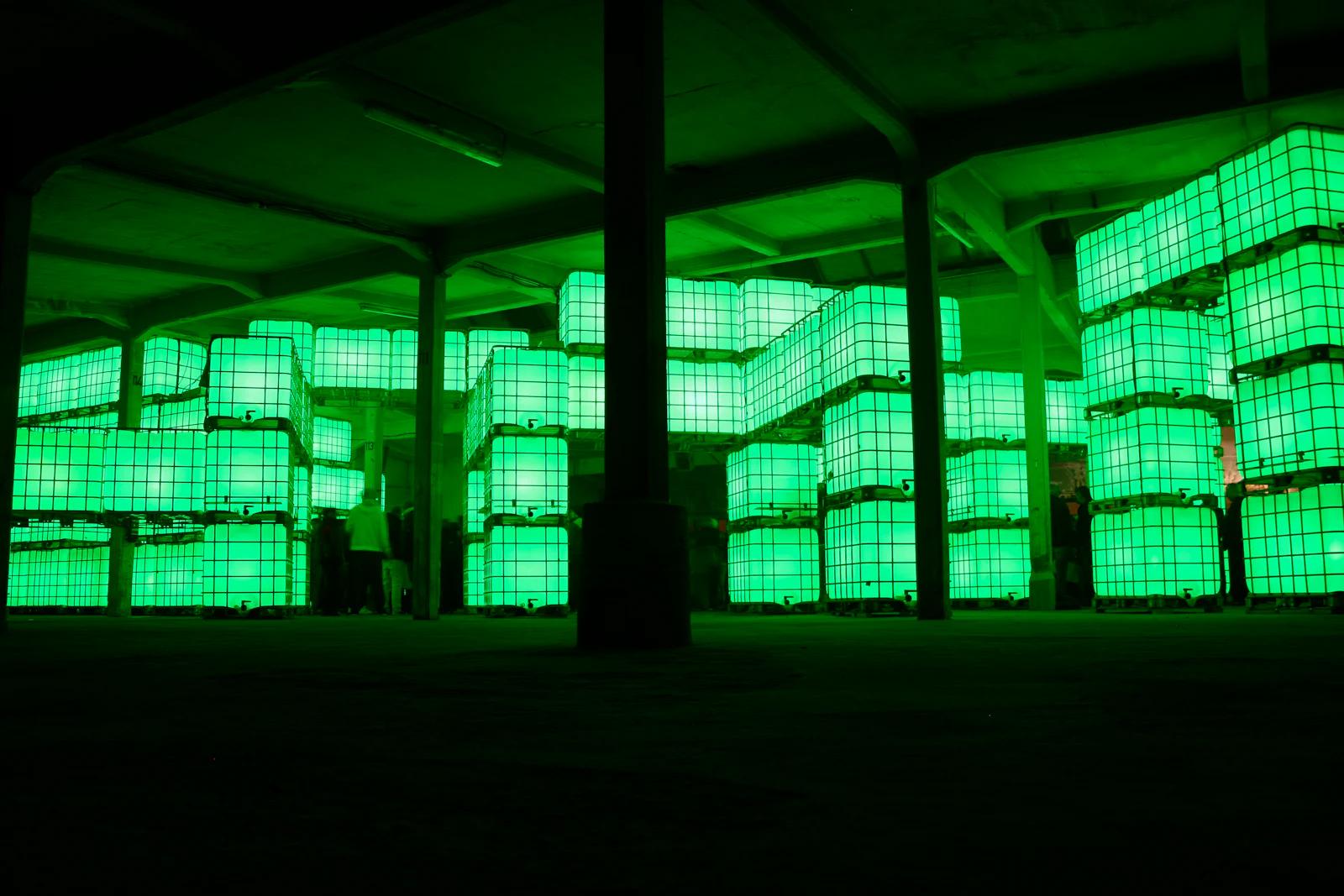 Stacked green lit forms in a dark industrial space.