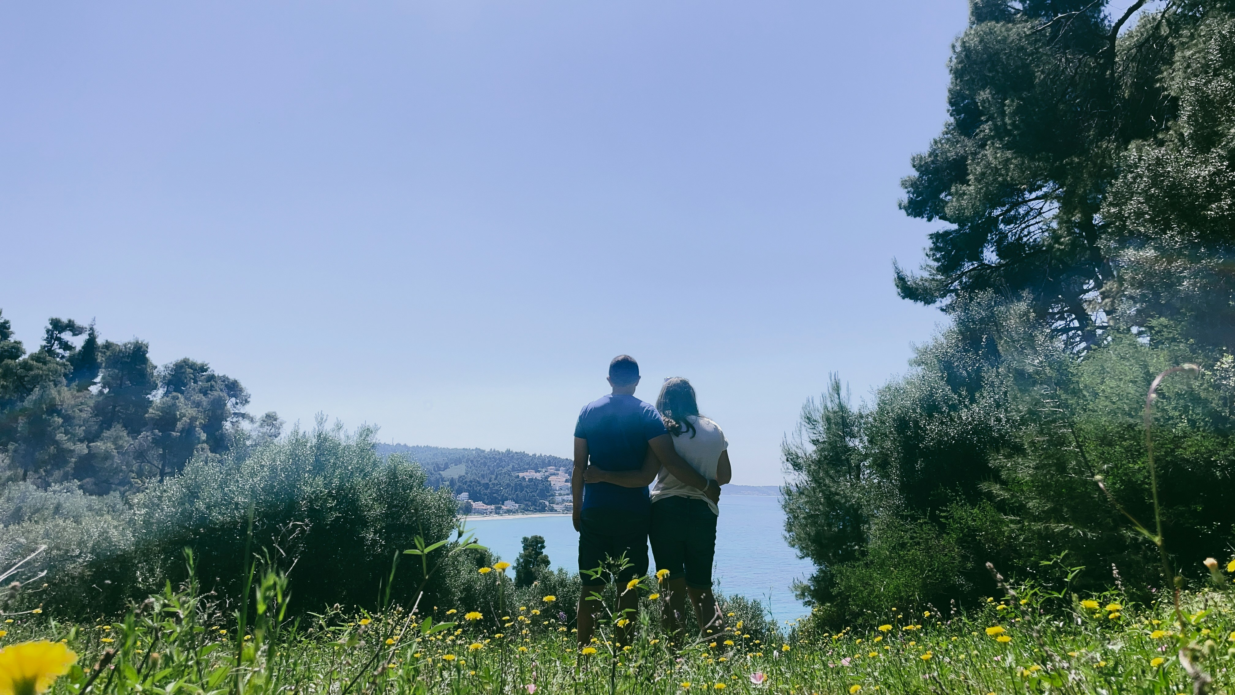 Two people stand overlooking the ocean under a clear sky.