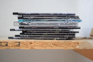 A stack of compact disc cases on a wooden shelf.