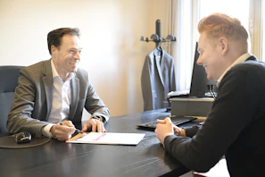 Two smiling men discussing documents at an office desk.
