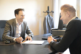 Two smiling men discussing documents at an office desk.
