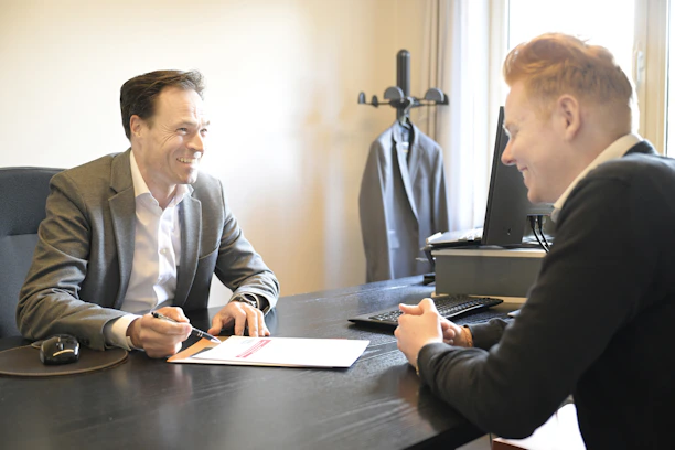 Two smiling men discussing documents at an office desk.