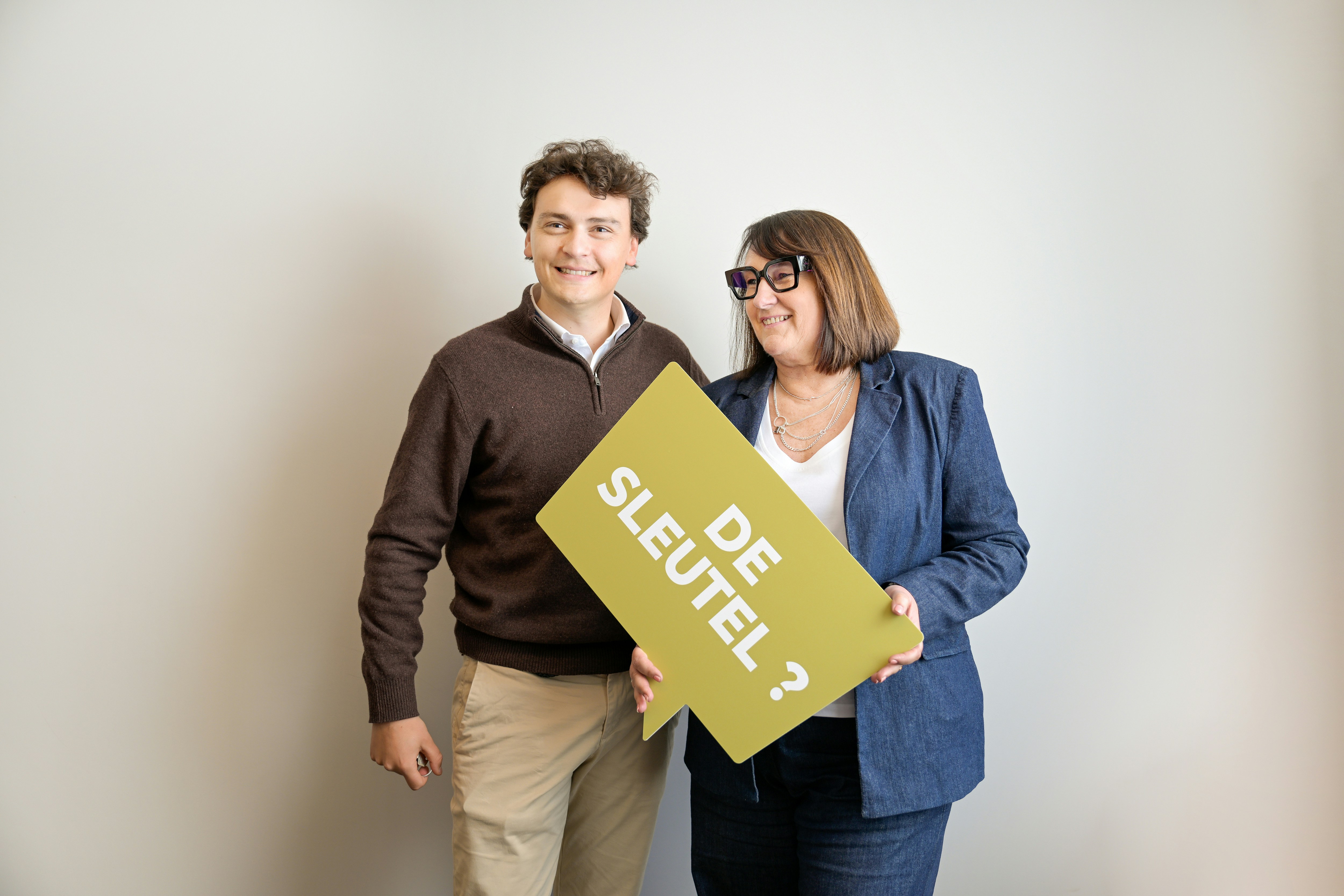 A man and woman hold a "de sleutel ?" sign.