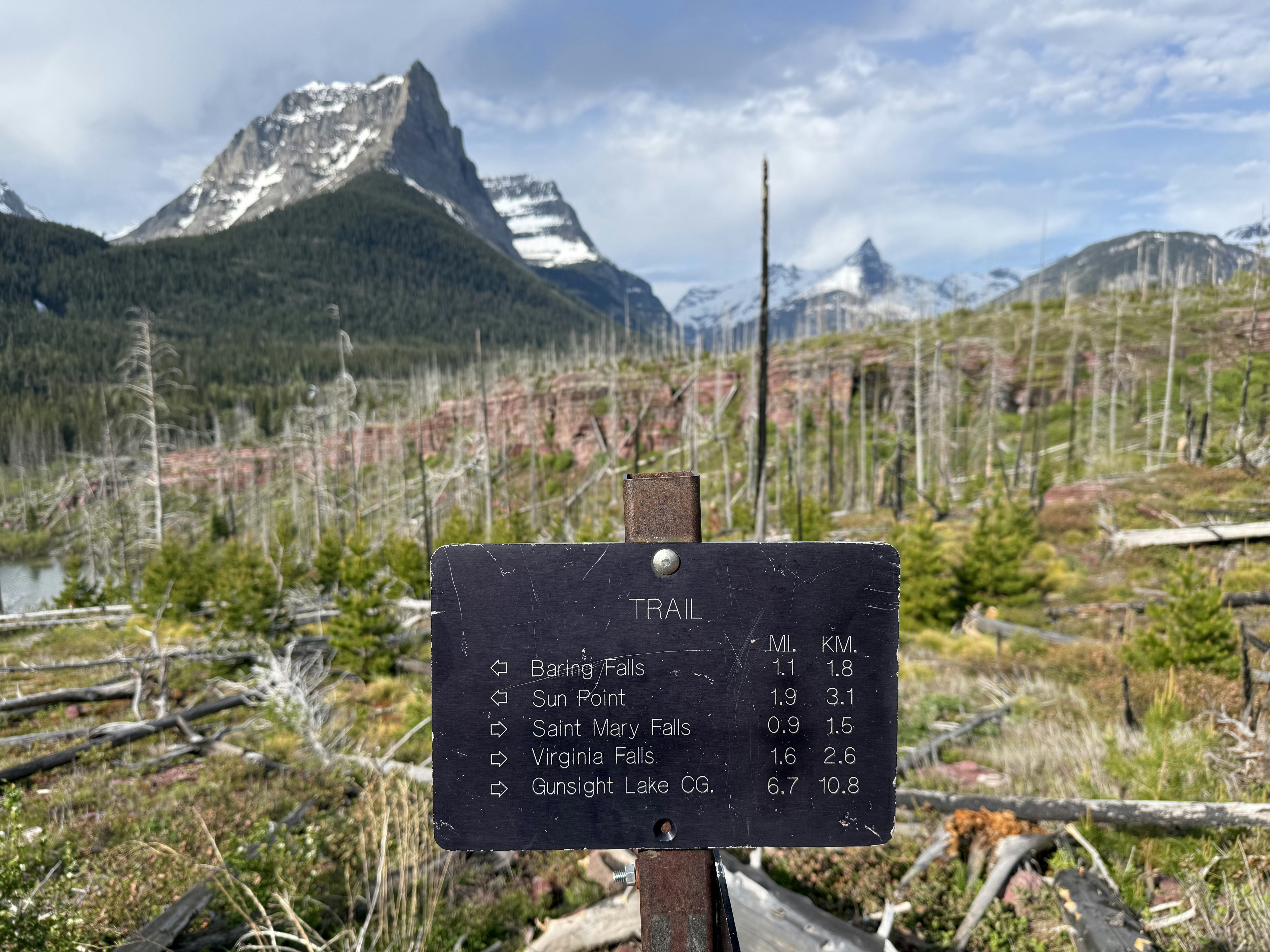 Ein Wegschild steht vor Bergen und einem Wald.