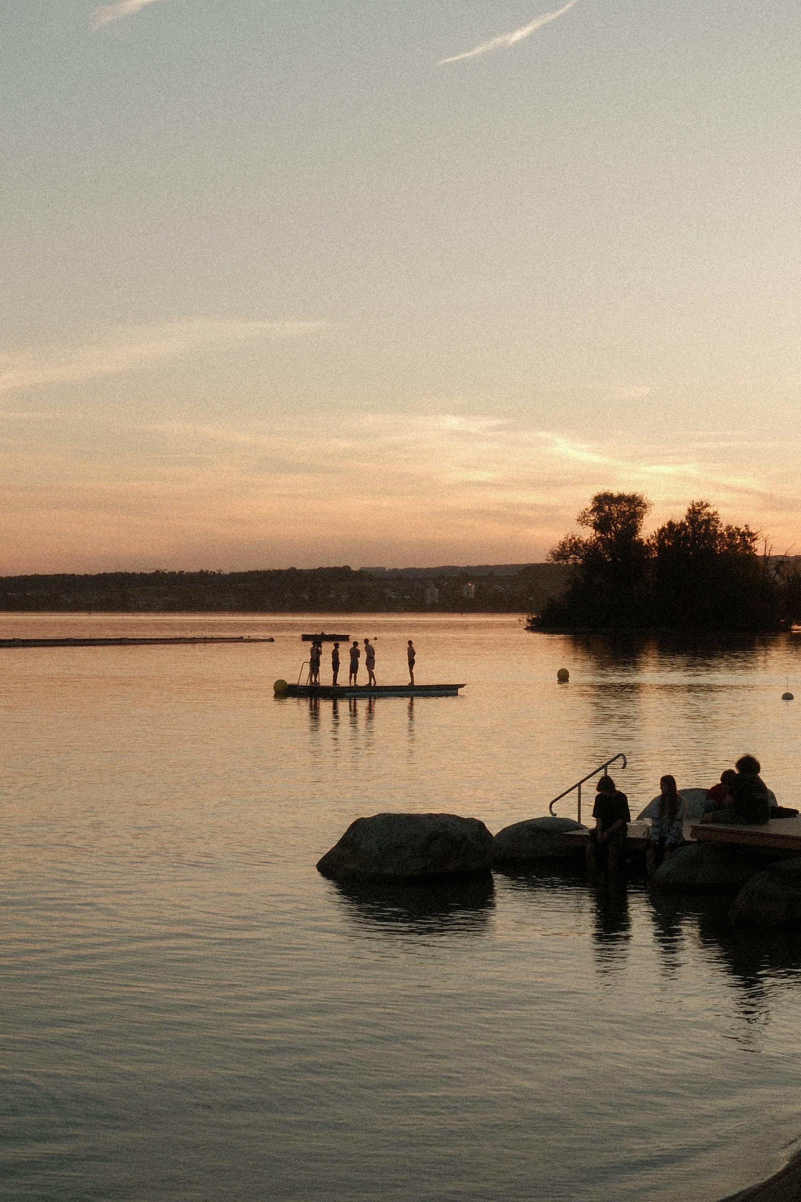 People on a floating platform and shore at sunset.