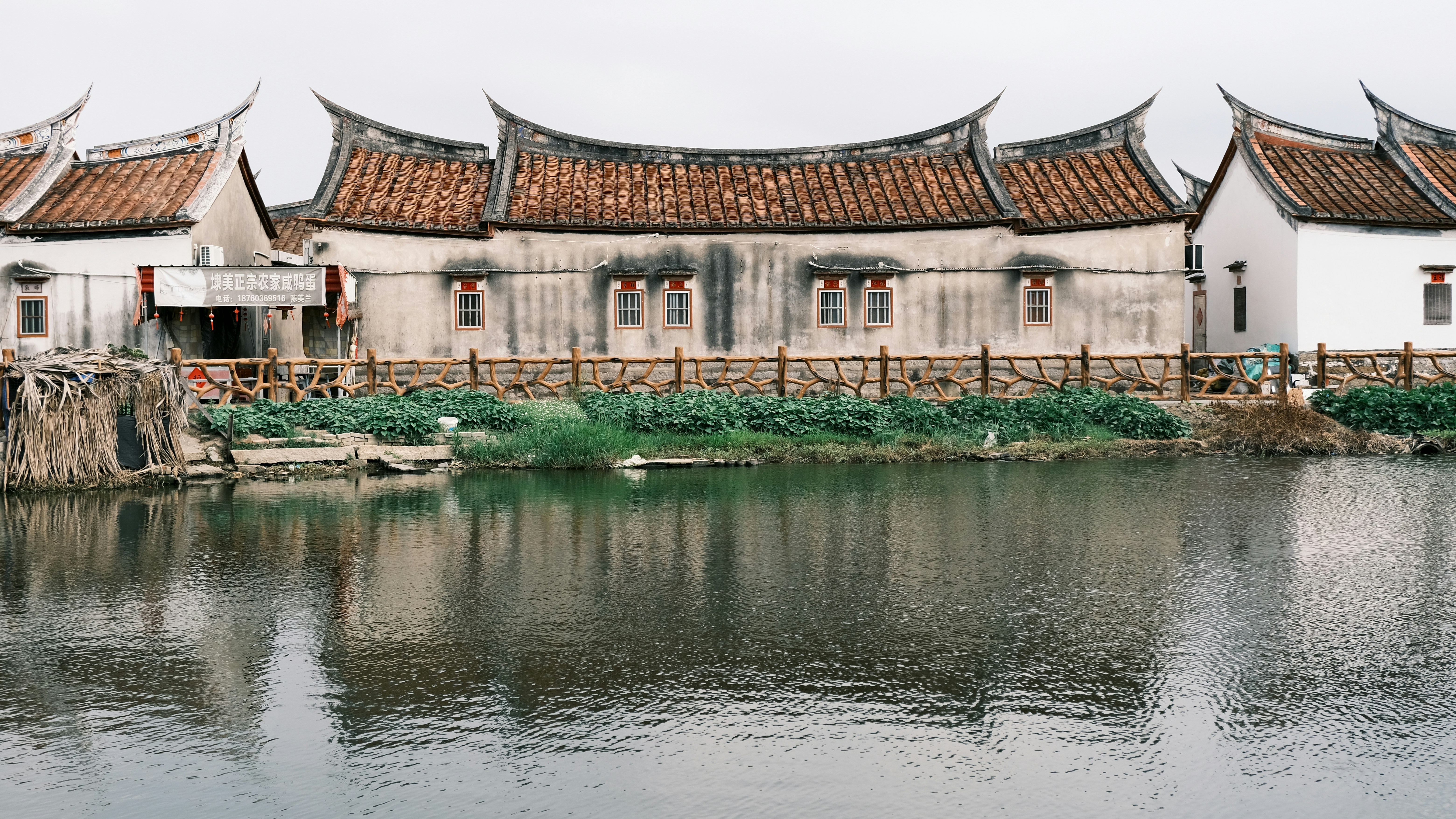 Traditional chinese buildings with curved roofs reflected in still water.