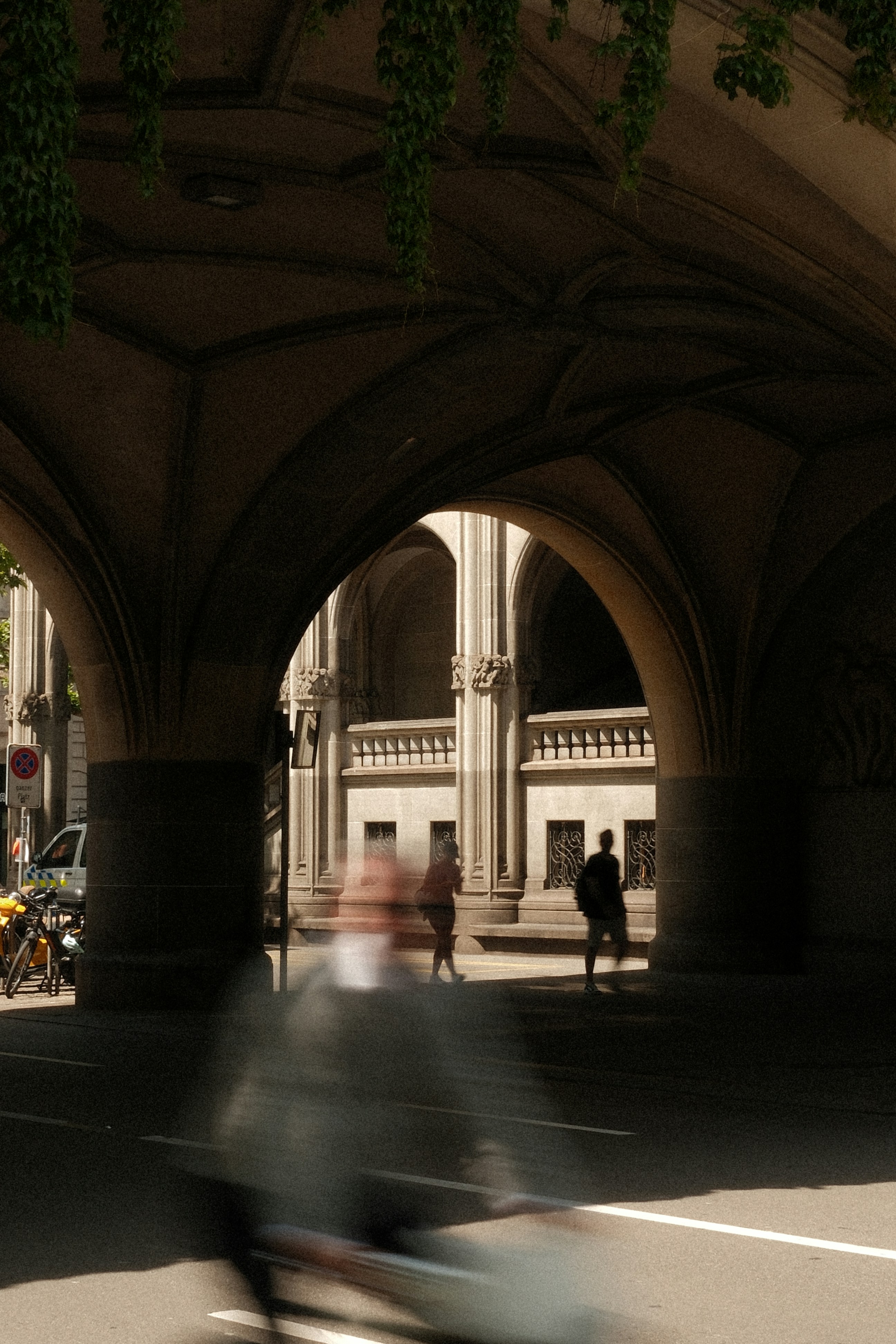 Motion-blurred cyclist passes under a historic stone archway.