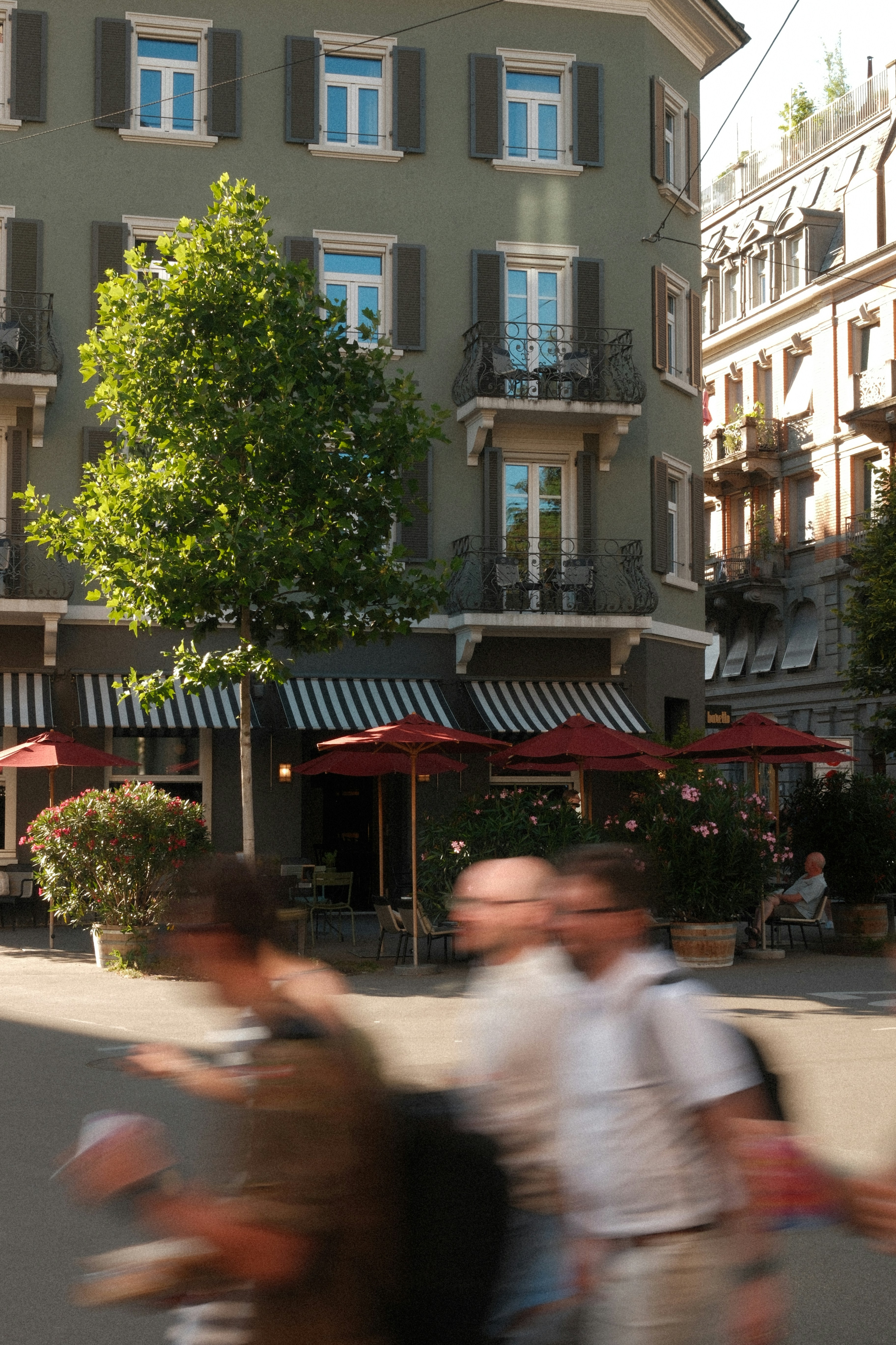 Blurred pedestrians pass a green building with a cafe.