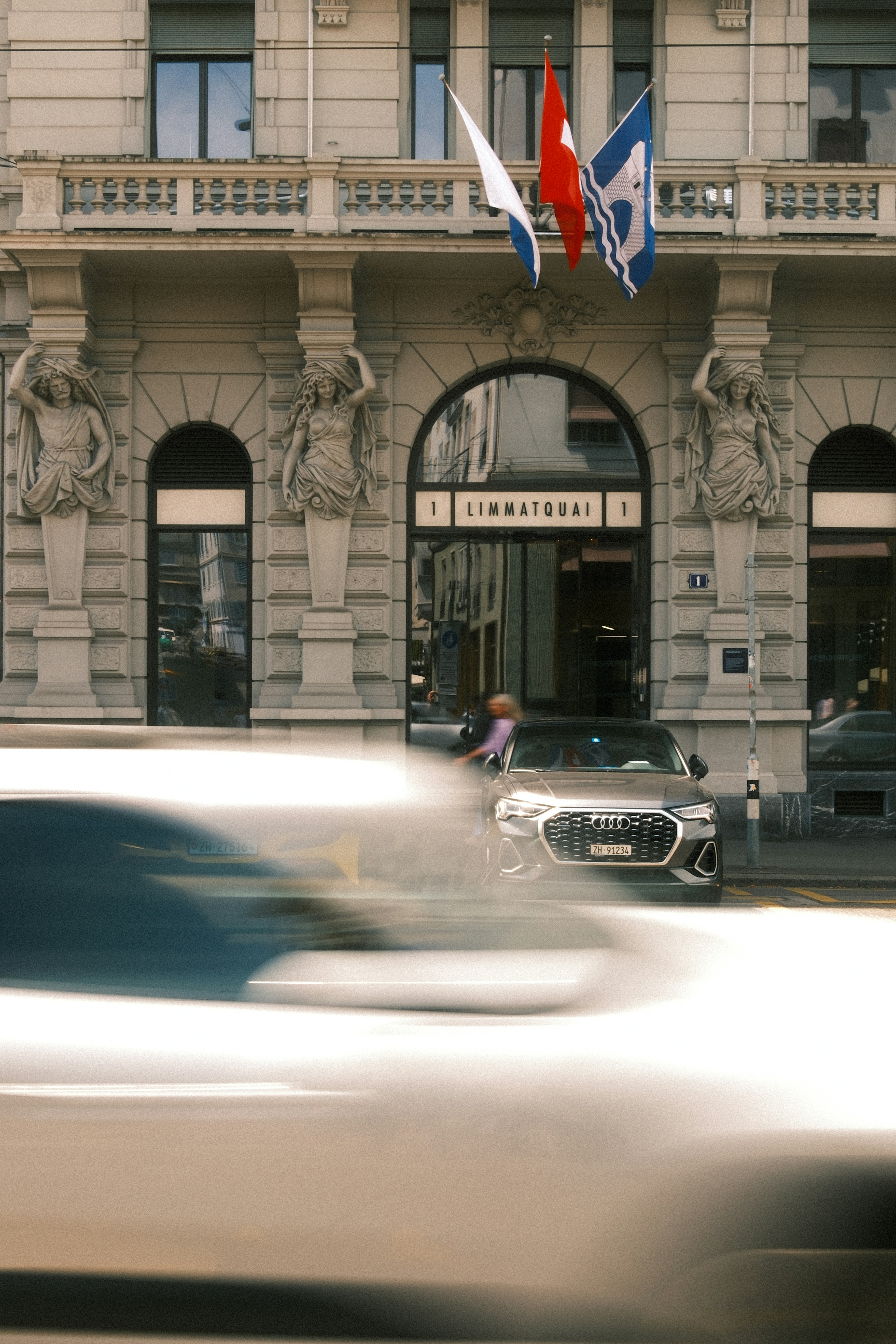 Ornate building with flags, parked car, and blurred motion.