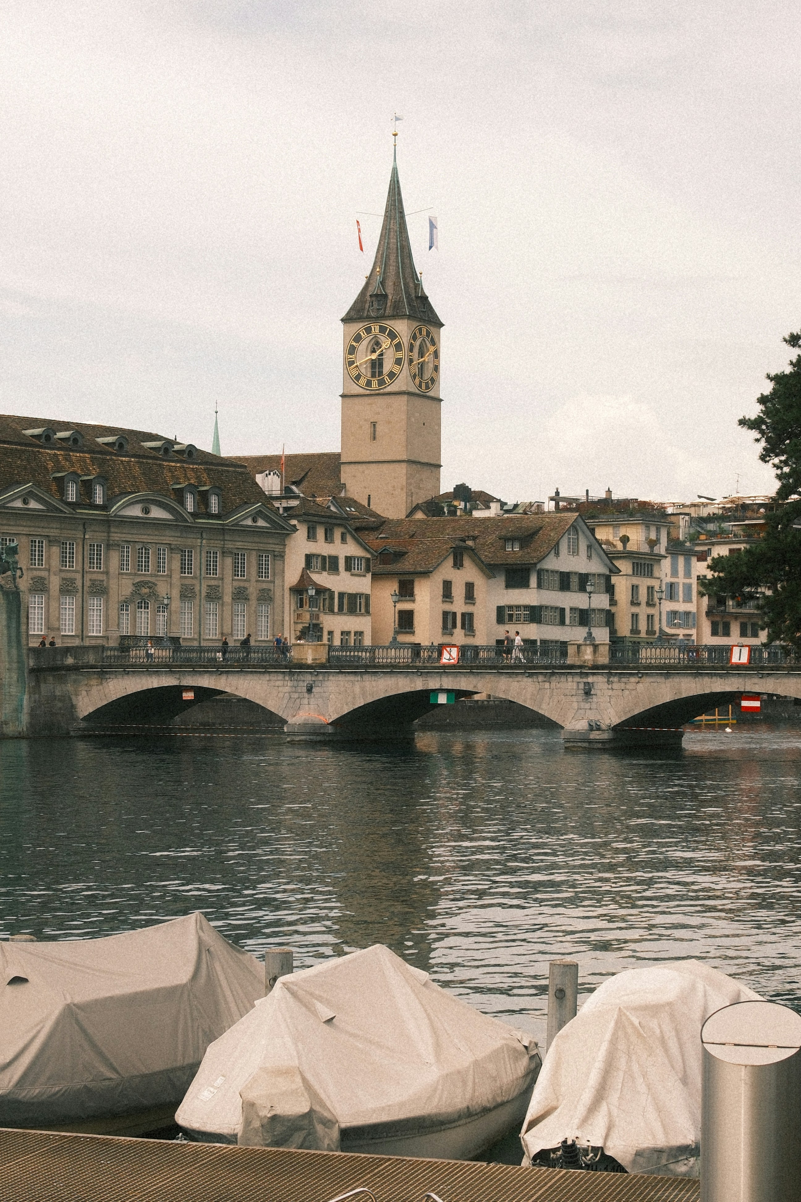 Clock tower, bridge, and covered boats on a city river.