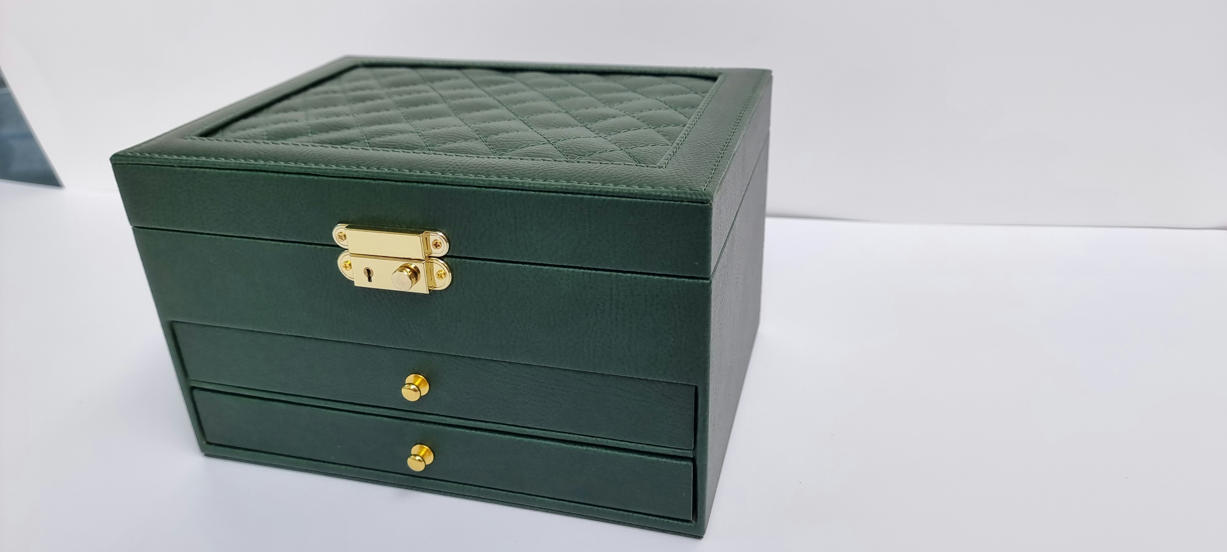 Elegante caixa de joias verde escura com fecho e gavetas douradas.