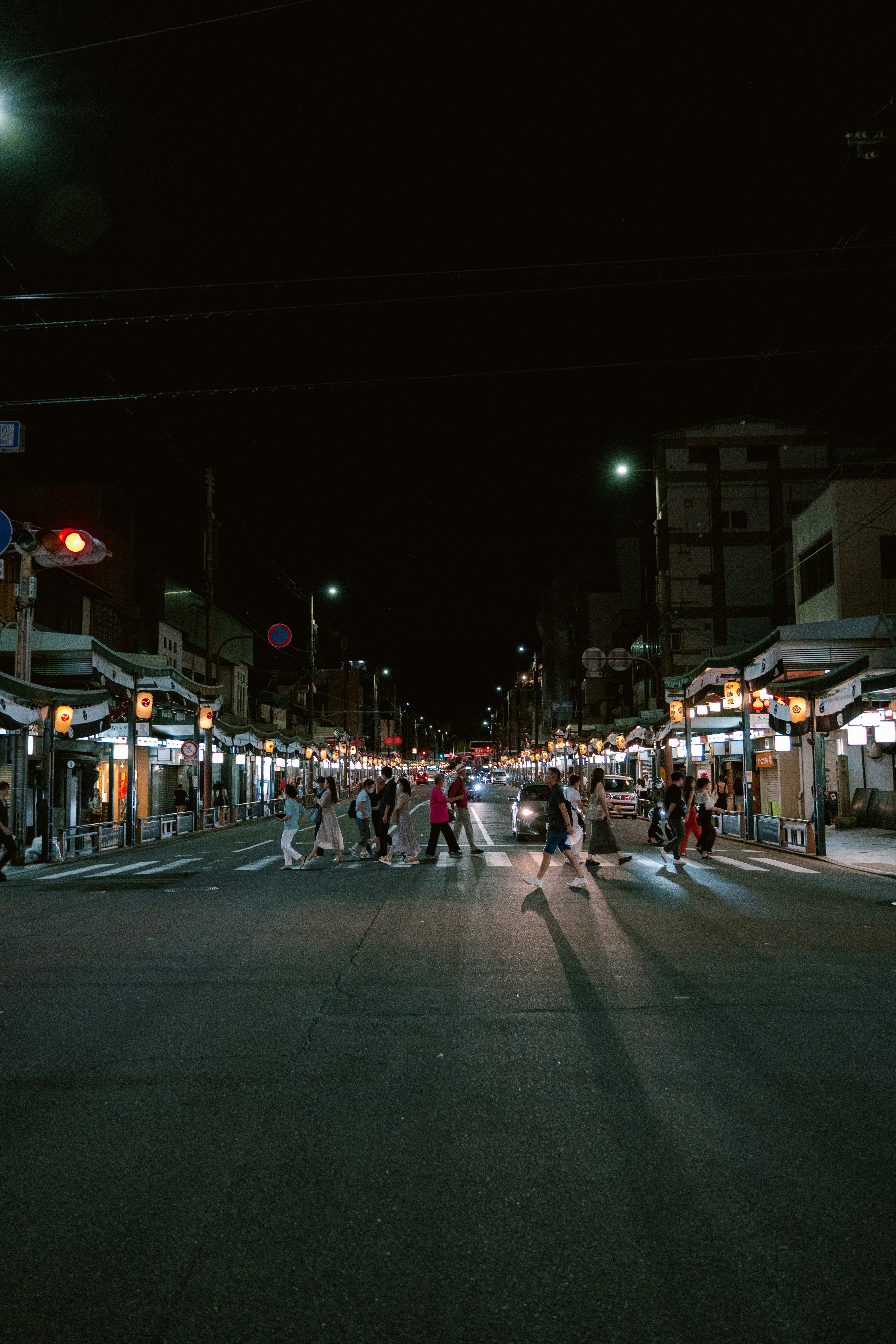 People crossing a busy street at night with illuminated shops.